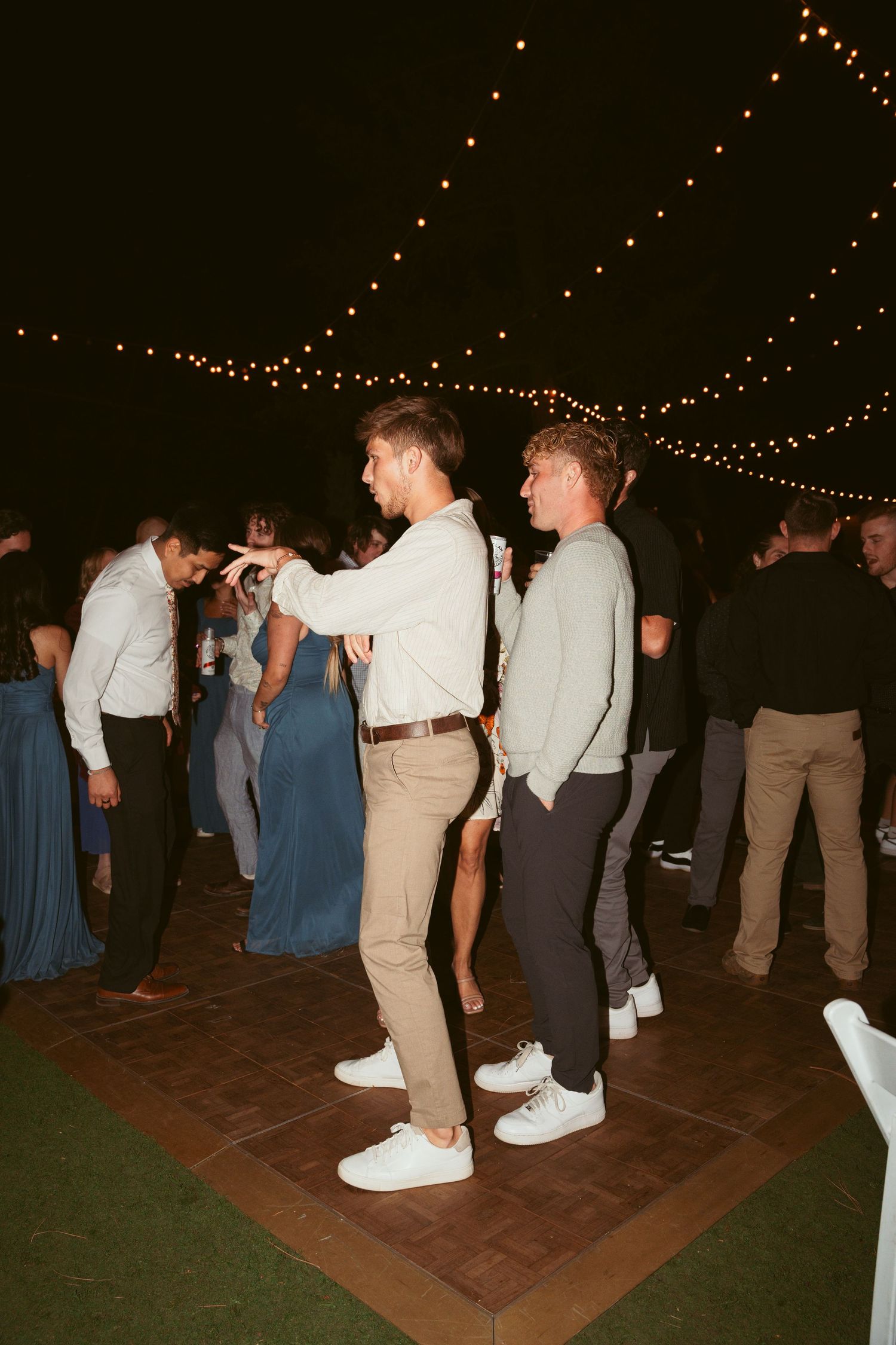 Wedding guests dancing in casual attire on an outdoor dance floor under string lights.