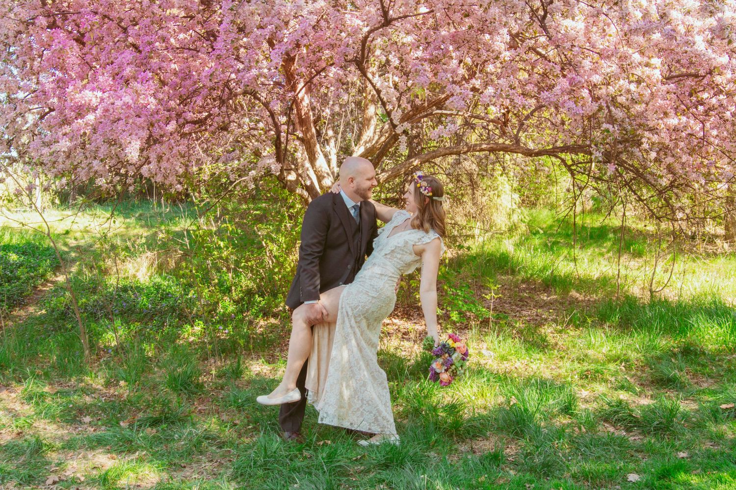 A couple poses beneath blooming cherry blossom trees in a spring garden.
