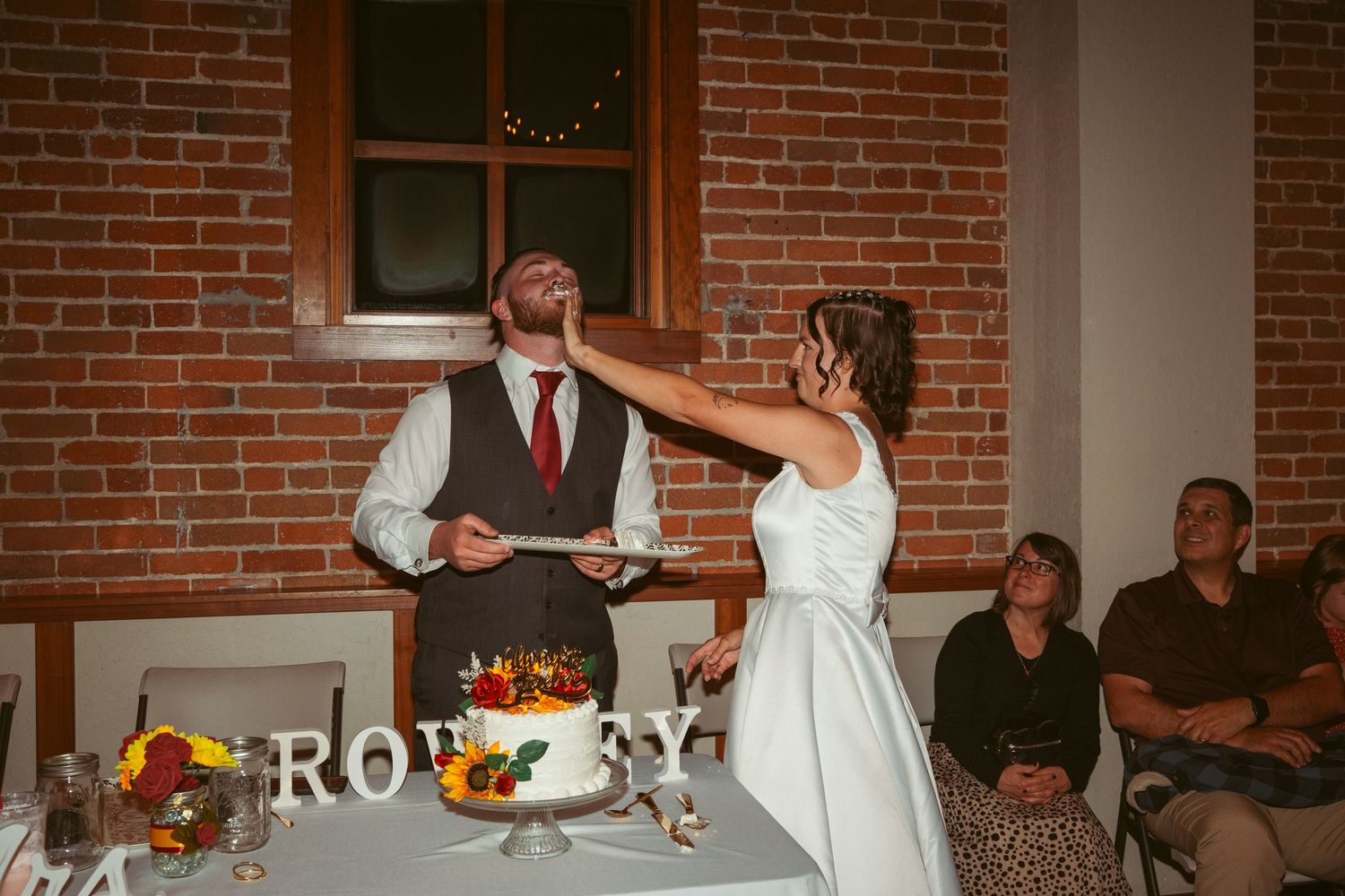 Bride playfully smears cake on groom's face during traditional wedding cake cutting ceremony.