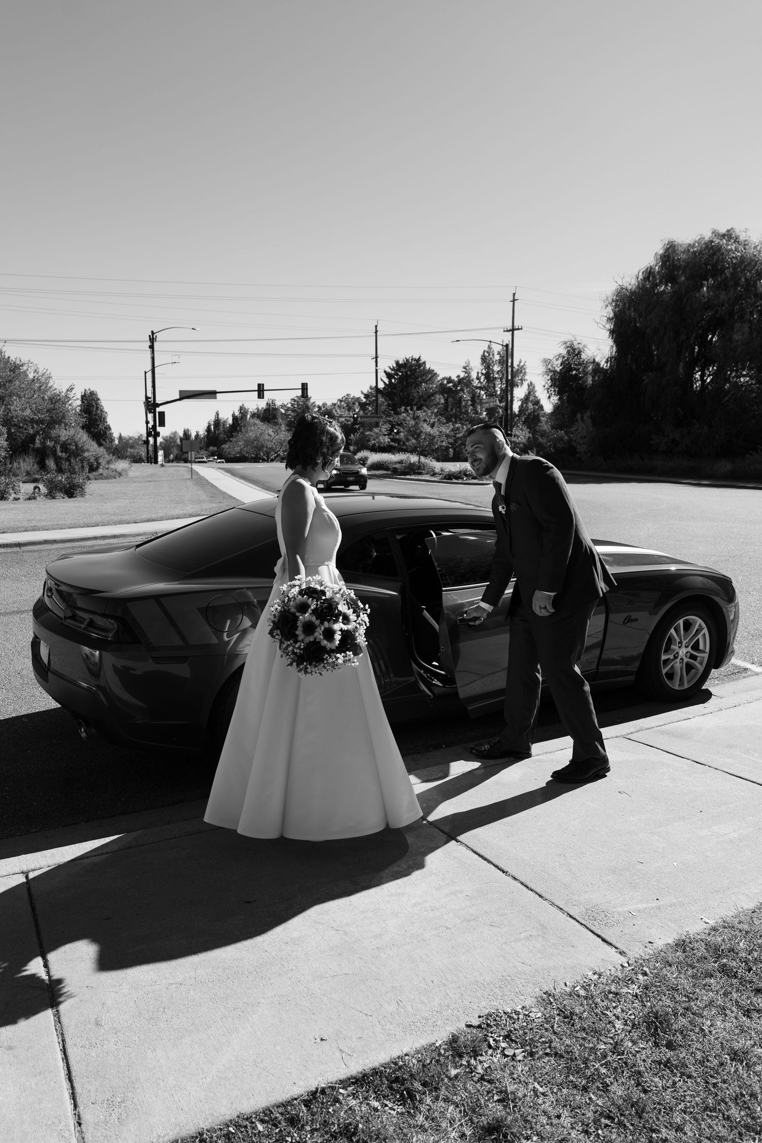 Black and white series showing wedding couple entering luxury vehicle on sunny day.