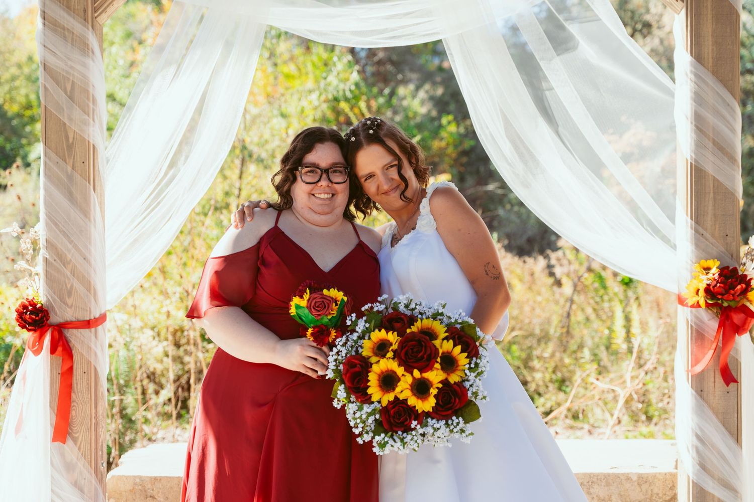 Wedding party poses under outdoor pavilion decorated with white fabric and red floral accents.
