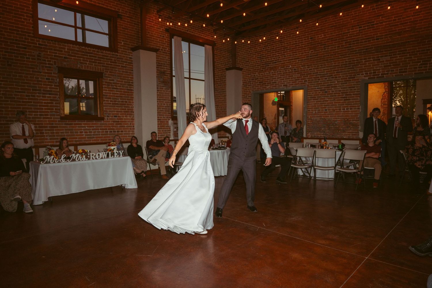 Dancers execute a graceful spin on the dance floor of a rustic brick venue with ambient lighting.