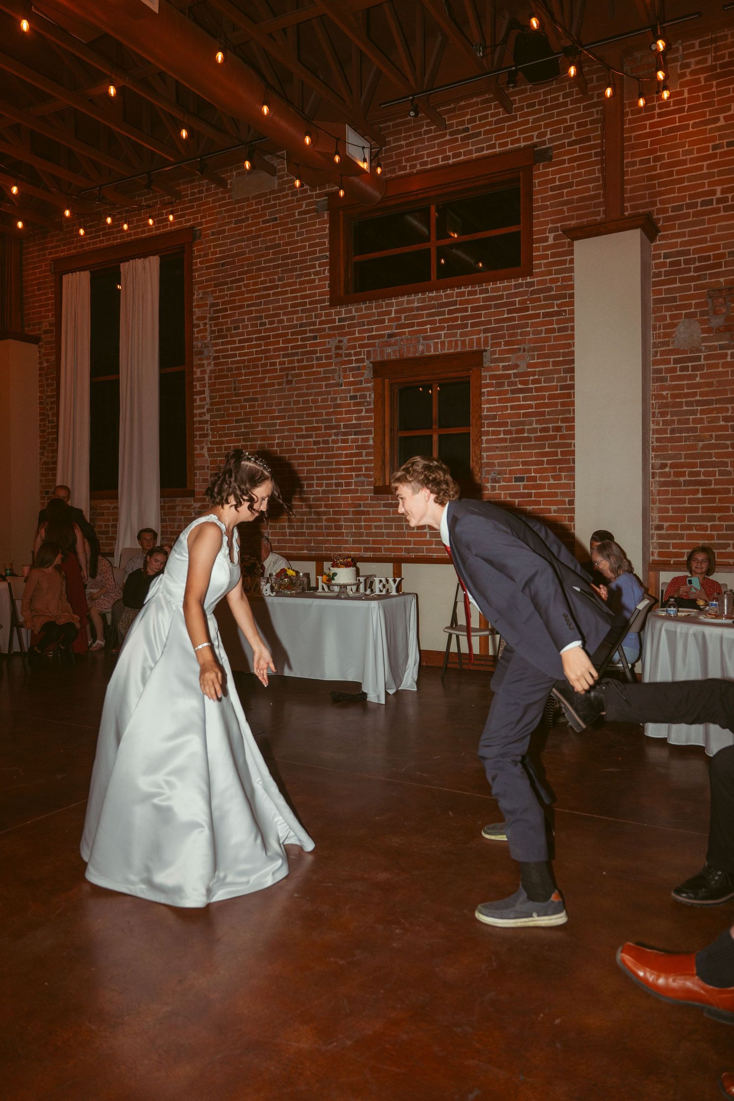 Wedding guests dancing in an industrial-style venue with exposed brick walls and string lights.
