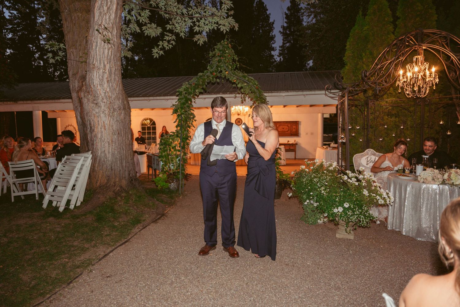 An evening outdoor wedding reception with elegant lighting and floral arrangements.