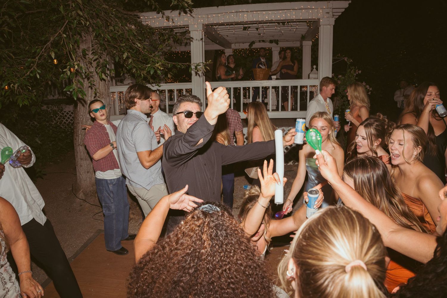 Energetic dancing and celebration at nighttime wedding reception under pergola.