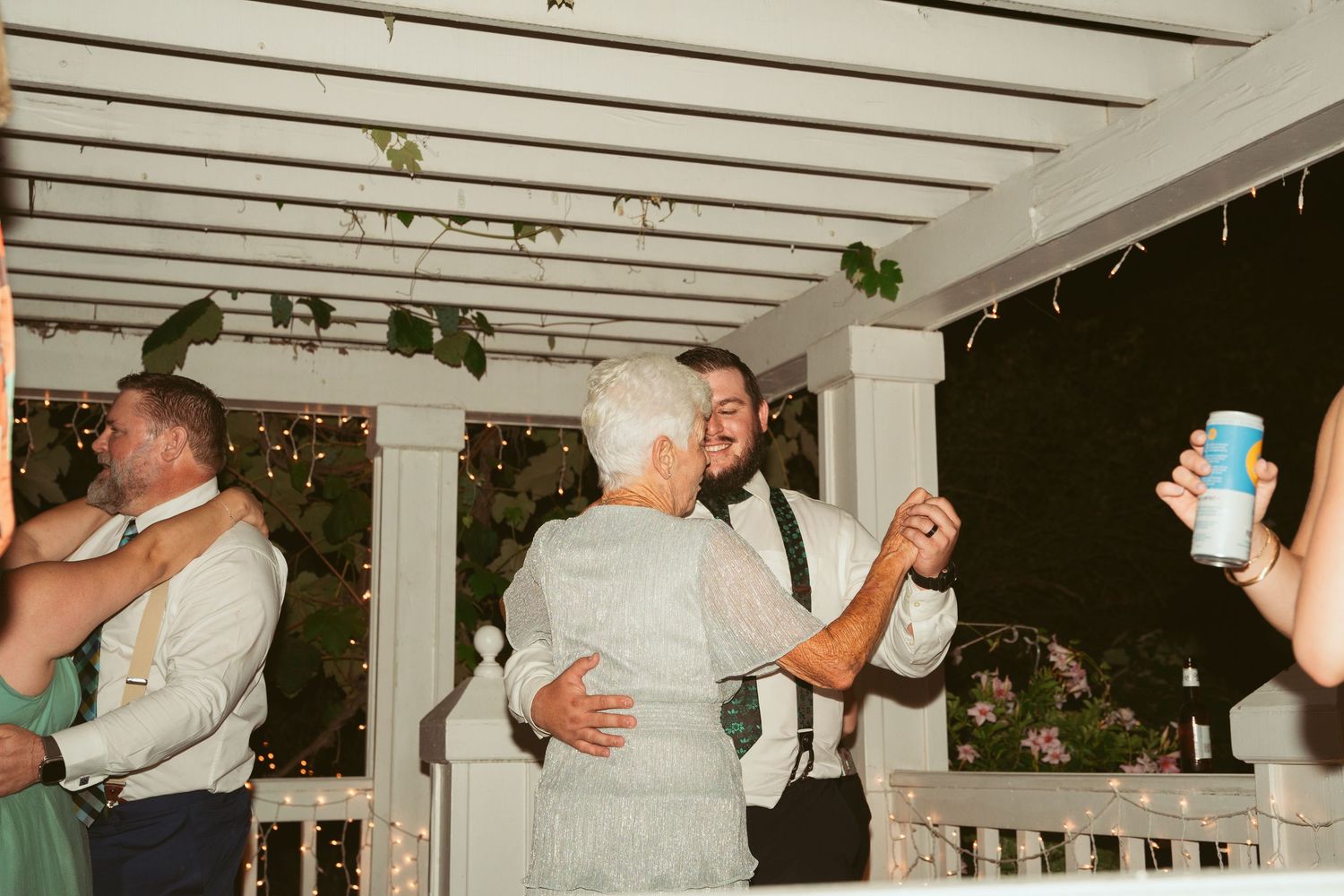 Wedding guests dancing under a white pergola at an outdoor reception.