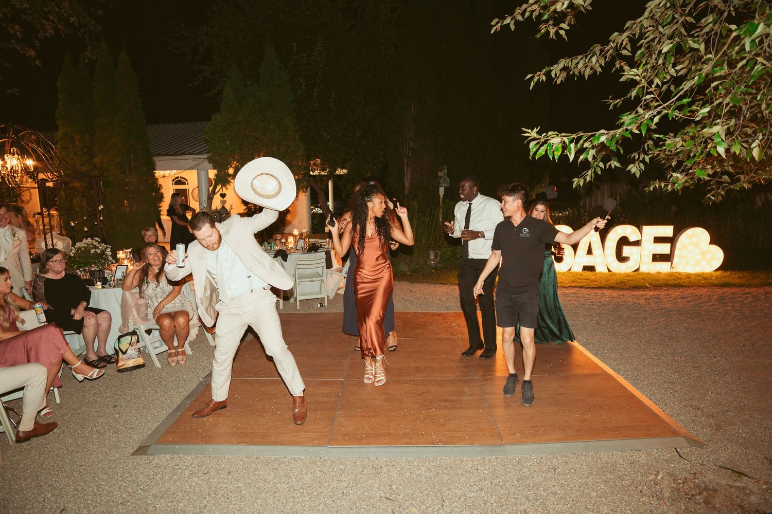 Wedding guests dance energetically on an outdoor dance floor at a nighttime reception.
