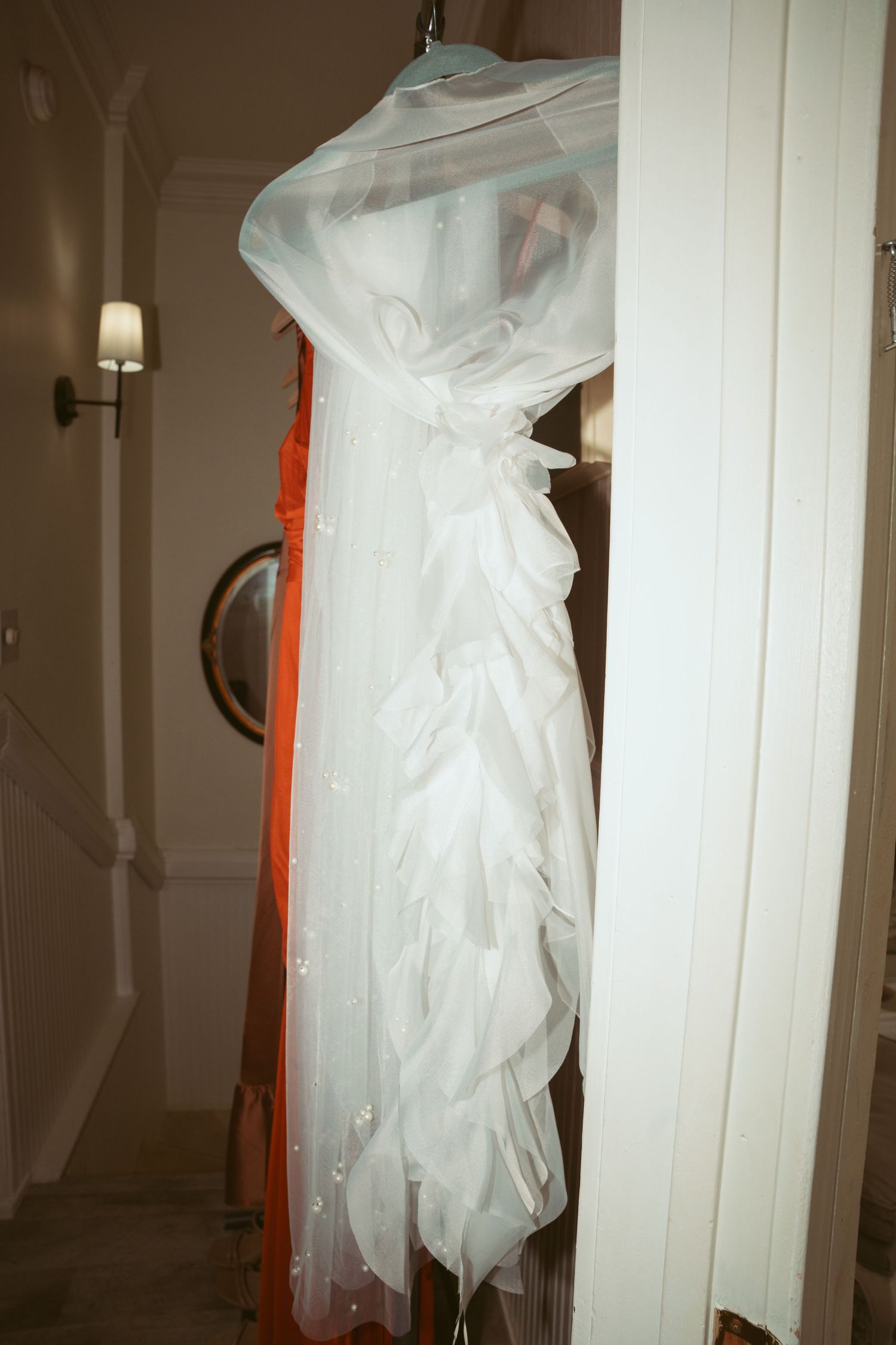 A white wedding dress hangs from a storage rack in a dimly lit room.