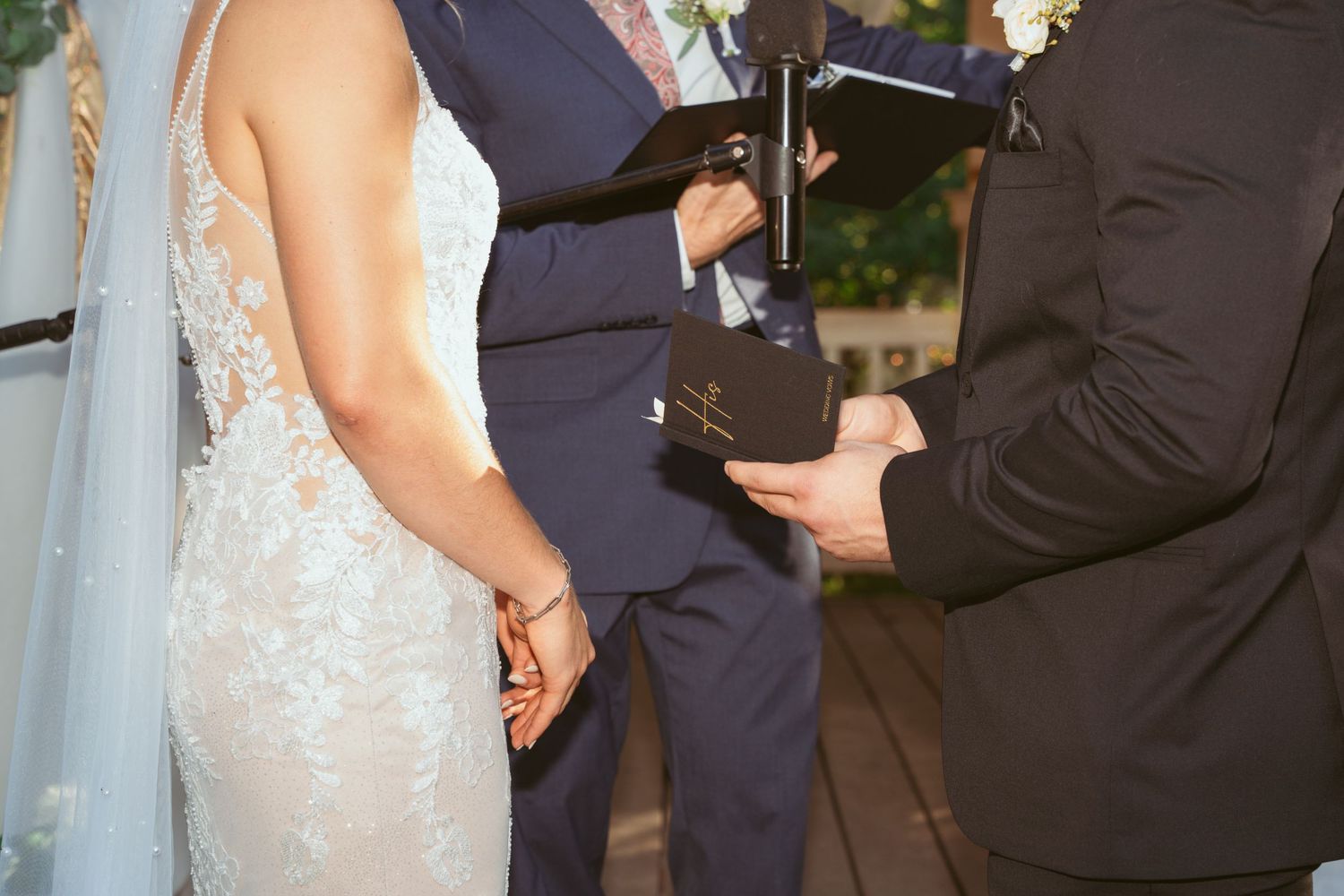 Bride and groom hold hands during outdoor wedding ceremony with white floral decorations.