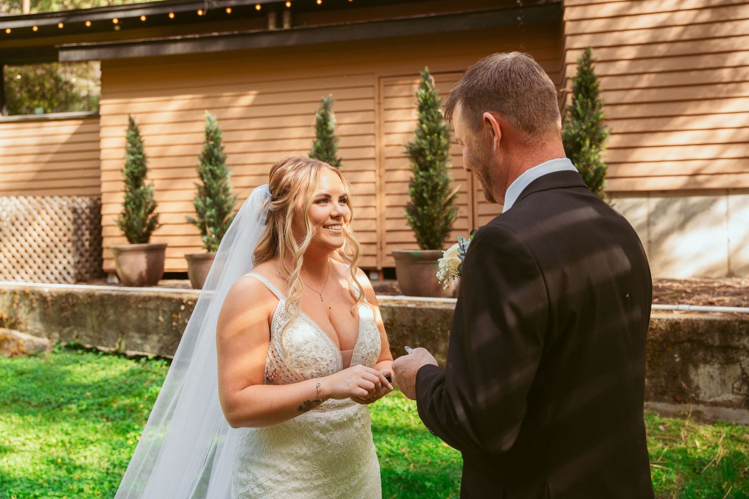 Couple in wedding attire dancing together in a sunlit garden setting with brick walls and greenery.