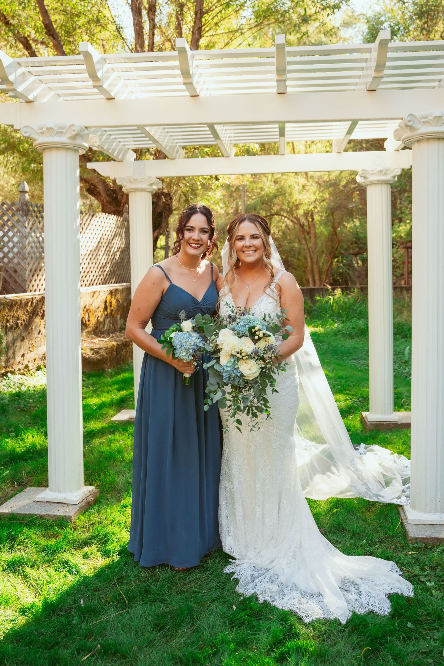 Wedding party poses under a white pergola in a garden with bridesmaids wearing navy blue dresses.