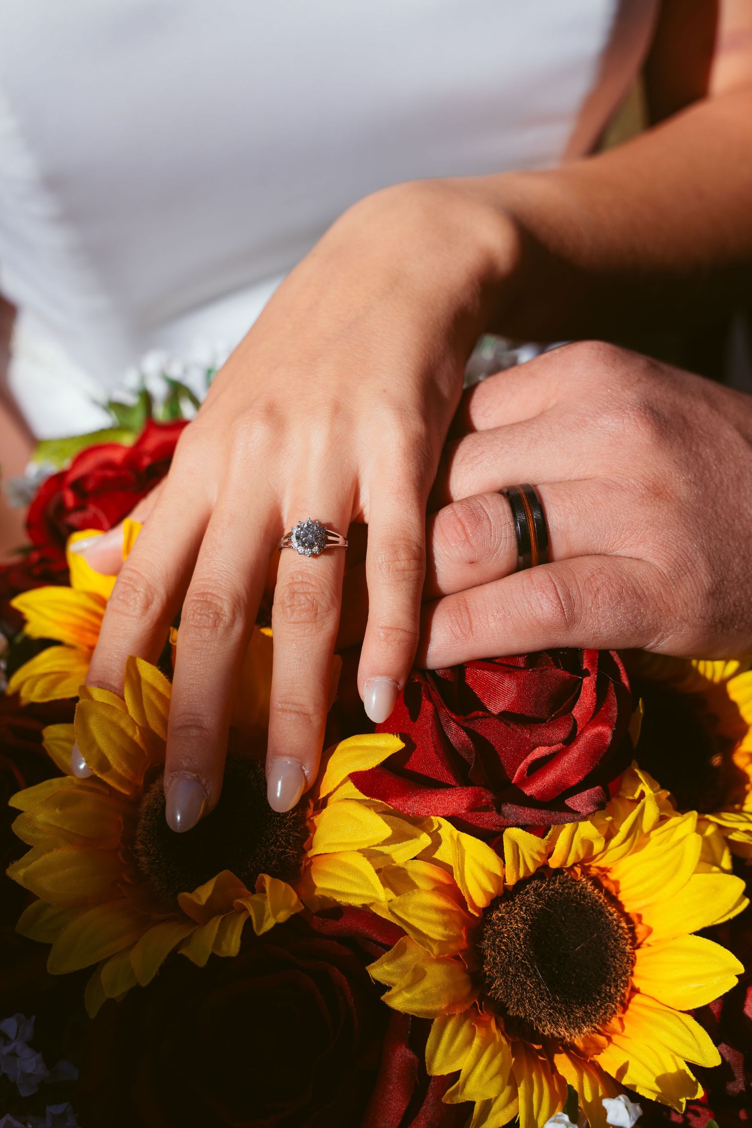 Close-up of hands with wedding rings touching sunflower and rose petals.