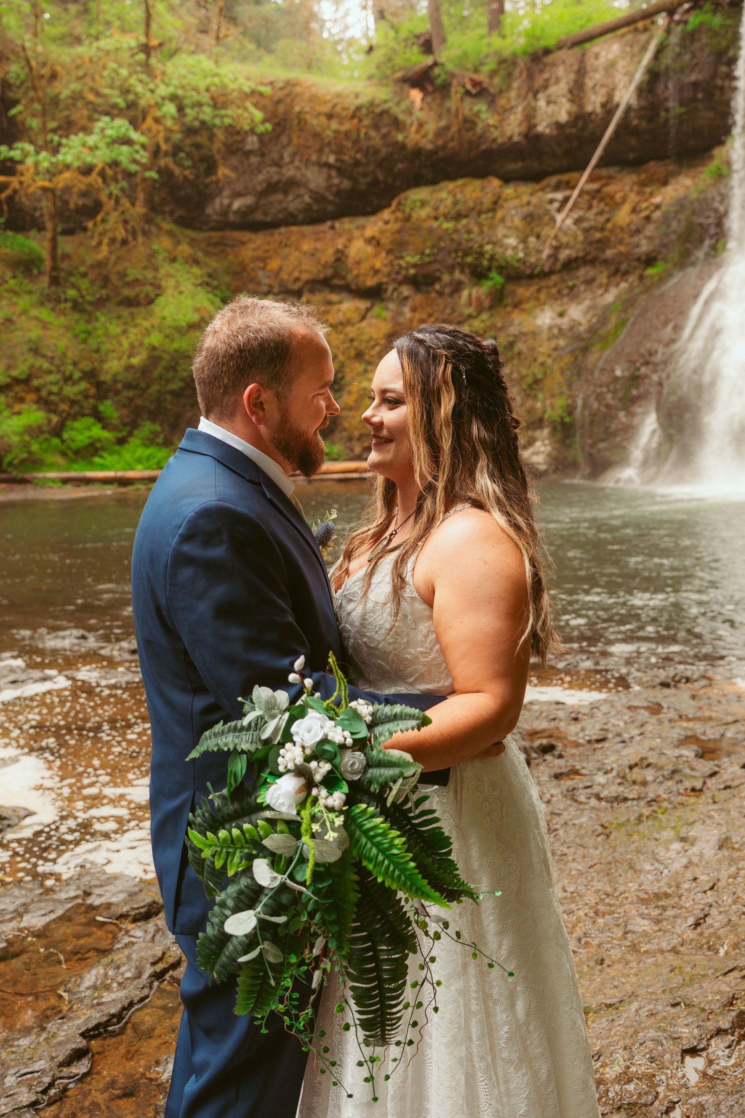 Wedding couple shares intimate moment in front of scenic waterfall.