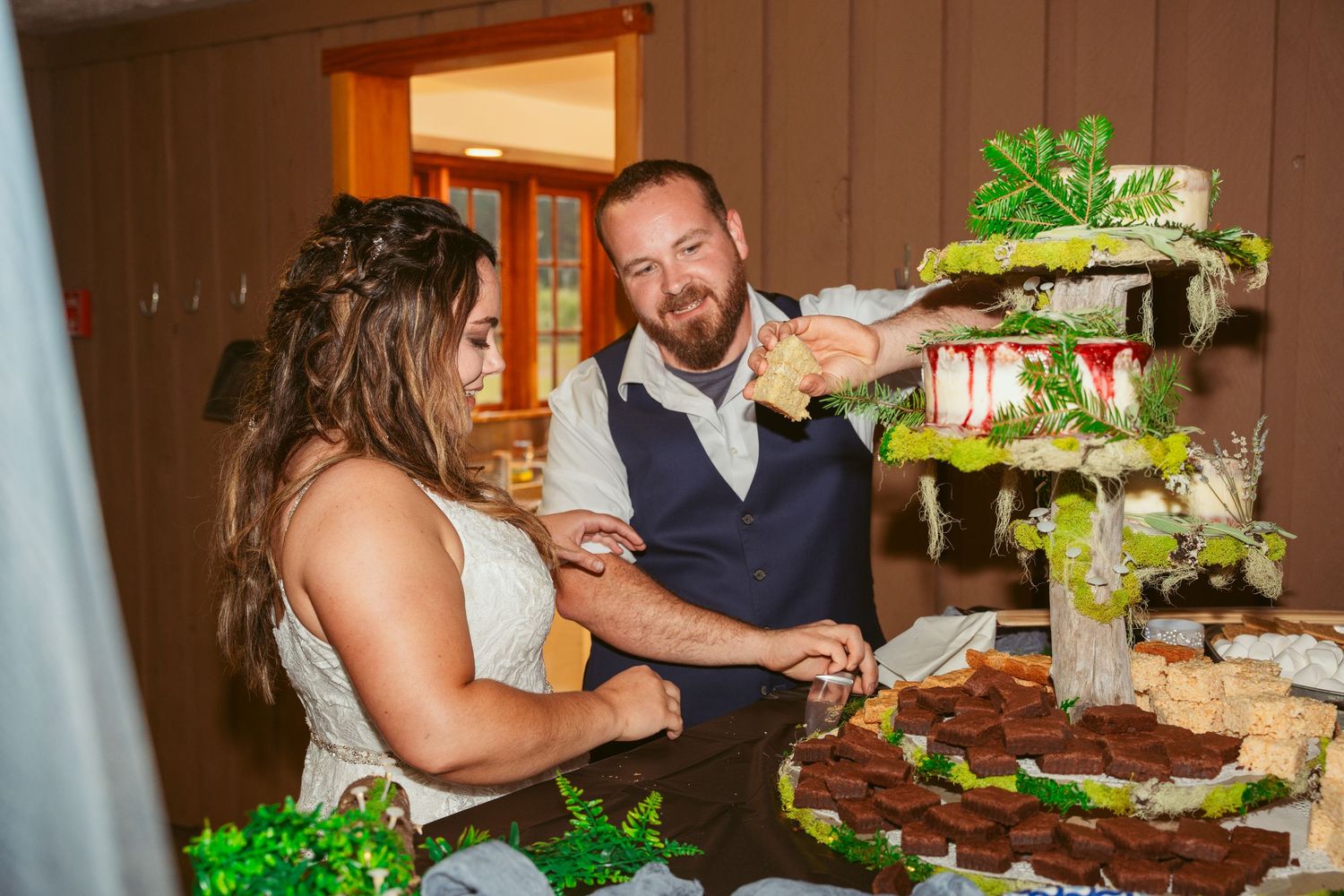 Wedding couple enjoying their cake-feeding tradition with laughter at indoor reception.