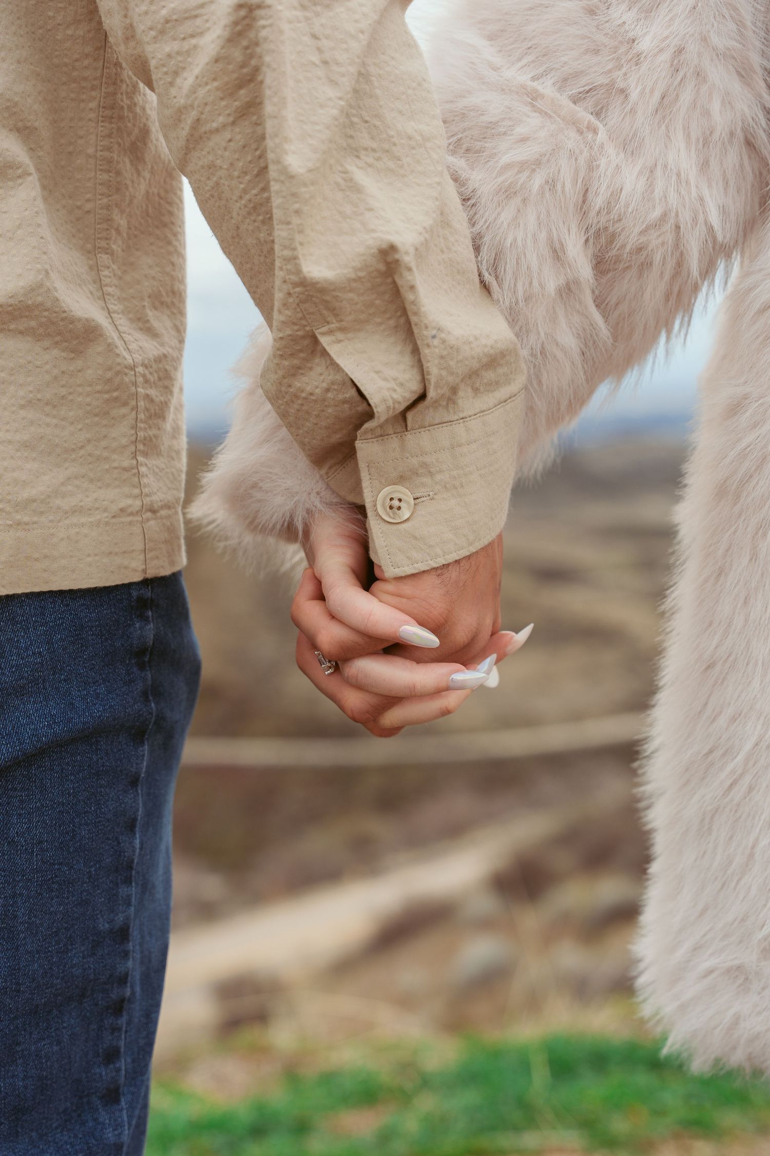 Close-up shot of two people holding hands while wearing beige and white clothing.