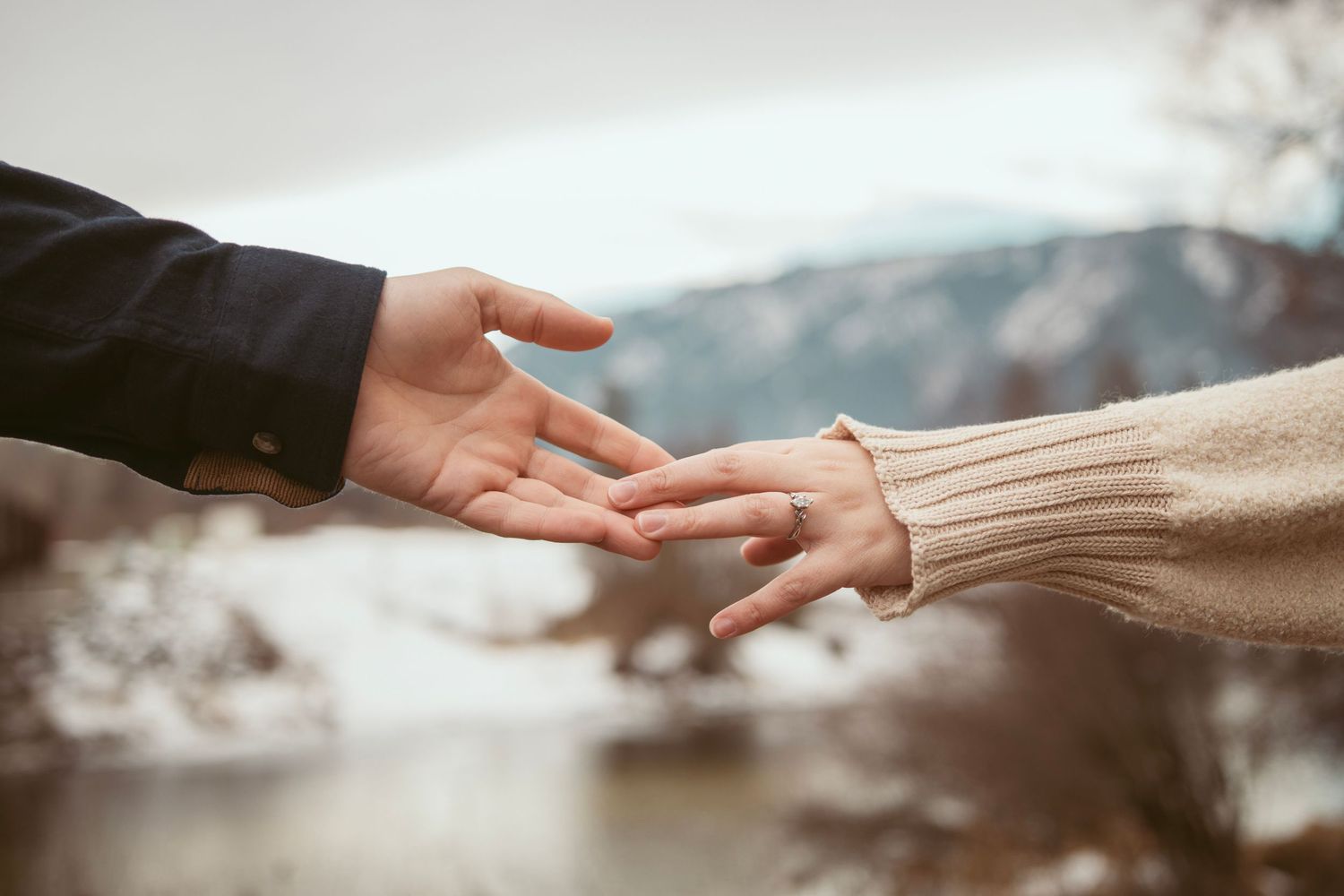 Two hands reaching towards each other against a blurred mountain landscape.