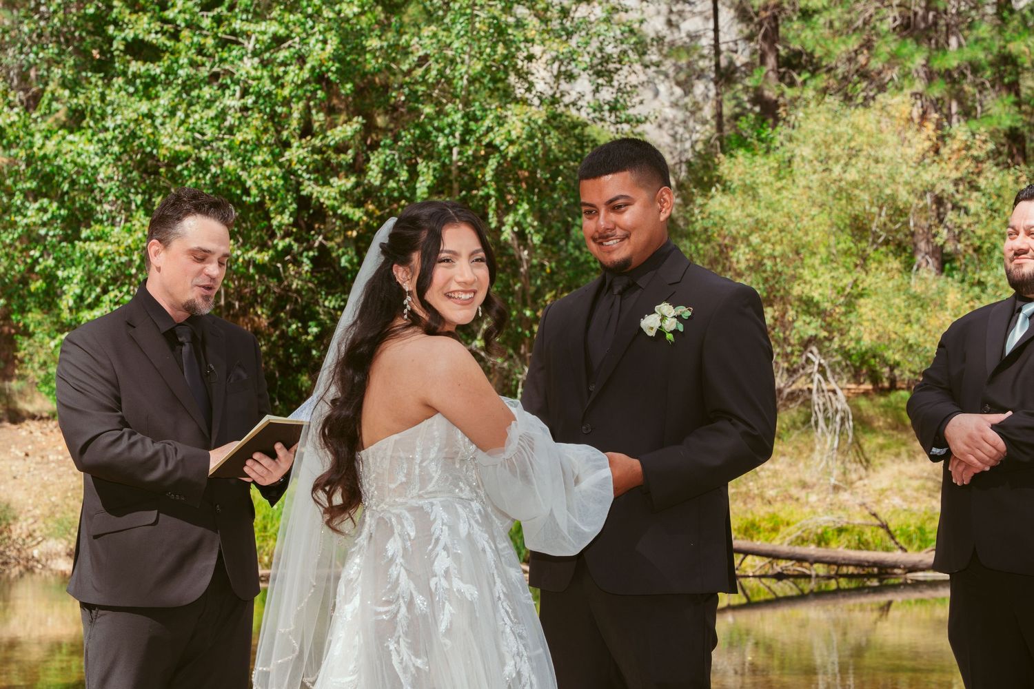 A wedding ceremony takes place in a lush green forest setting with natural lighting.