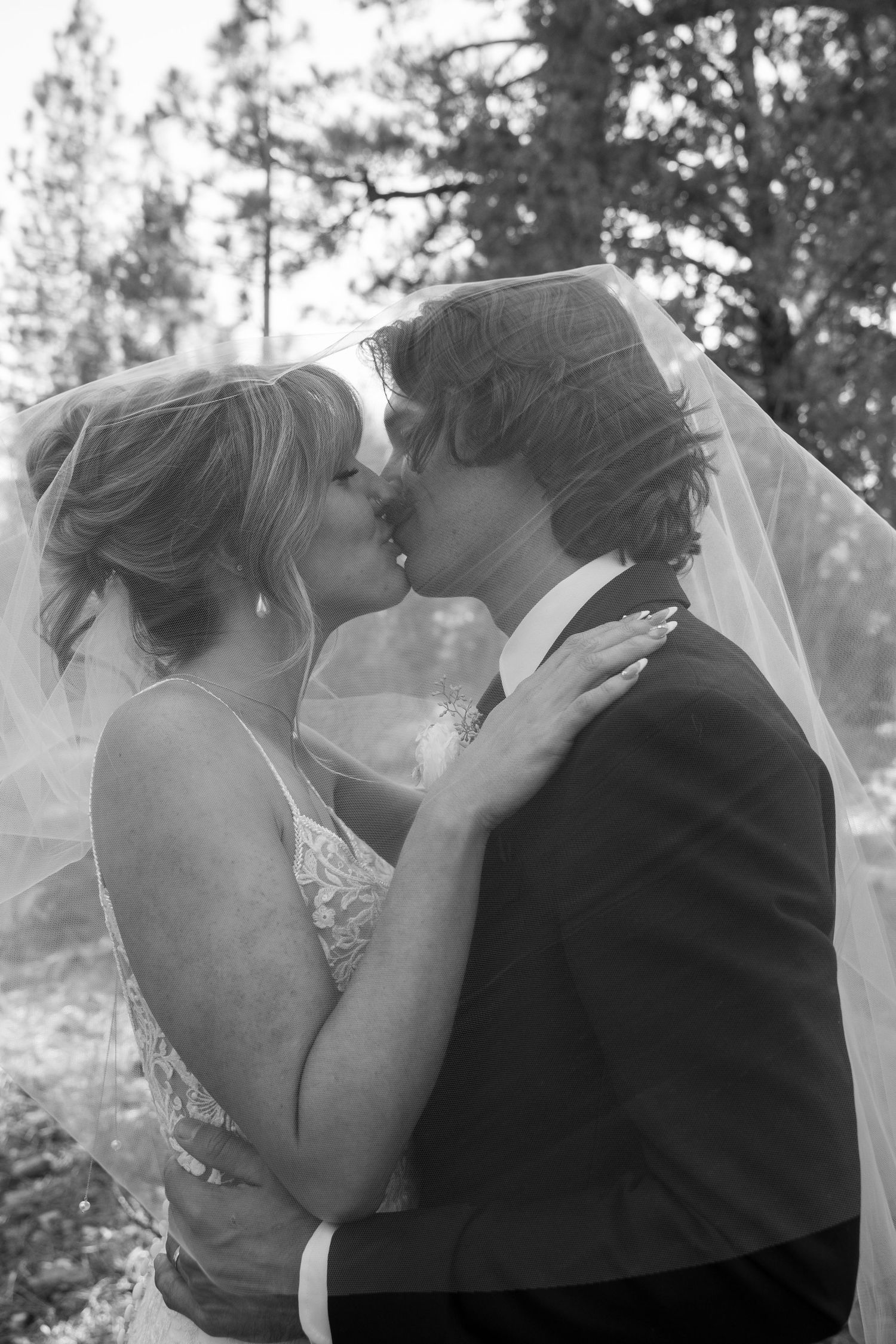 Black and white photo of a romantic wedding moment captured in a forest setting.