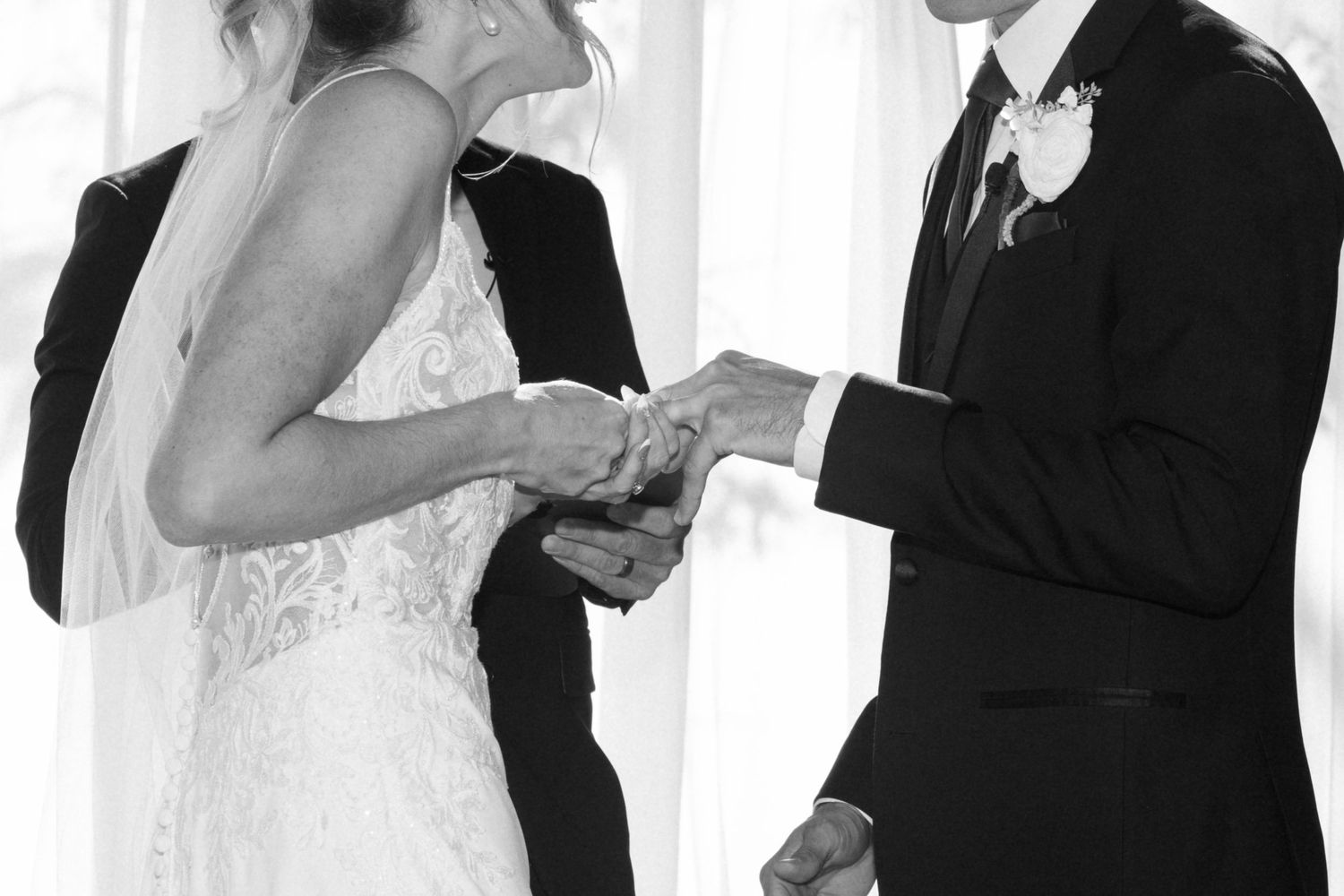 Black and white photo capturing an intimate moment during a ring exchange at a wedding ceremony.