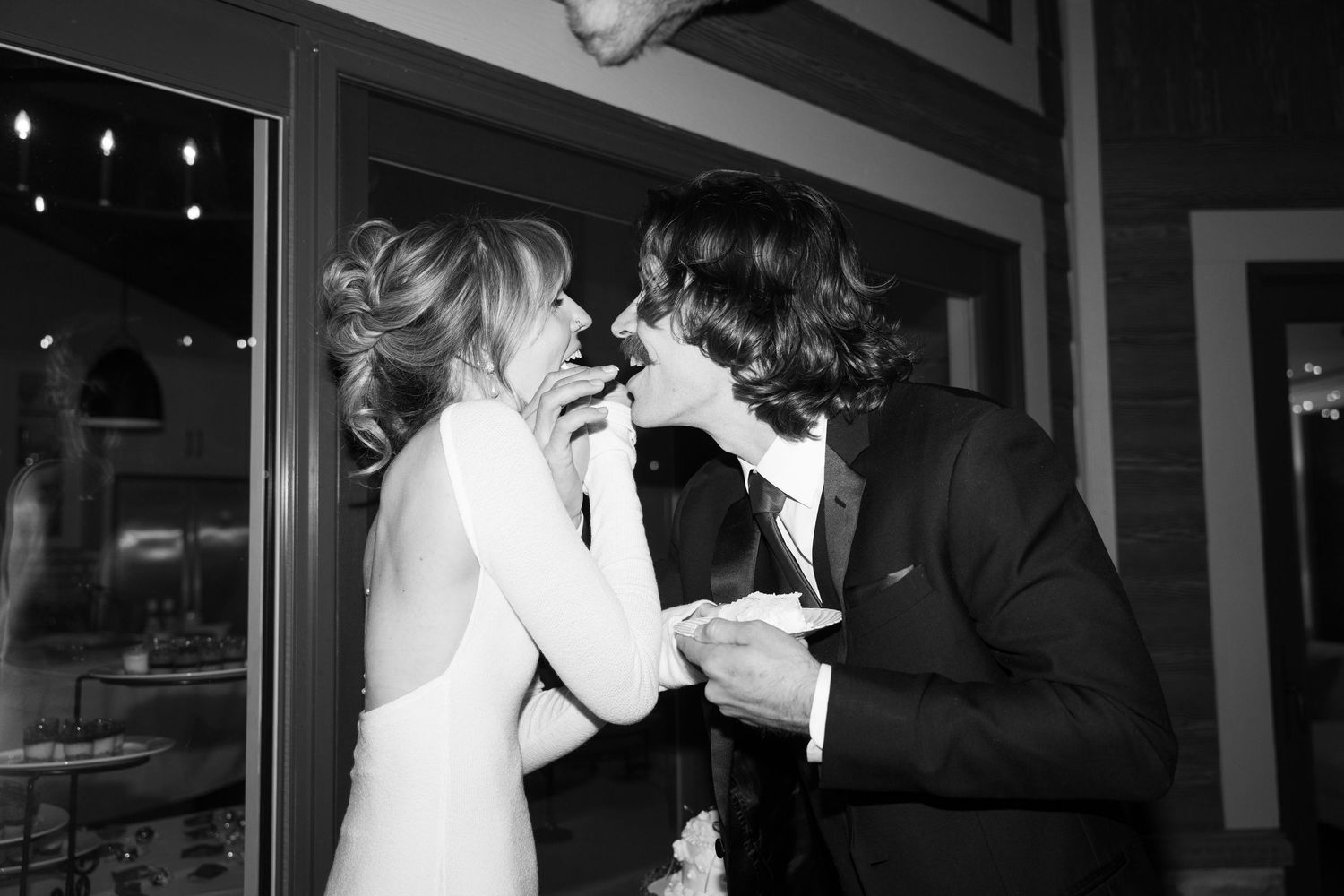 Intimate black and white photo of couple sharing cake at their wedding reception.