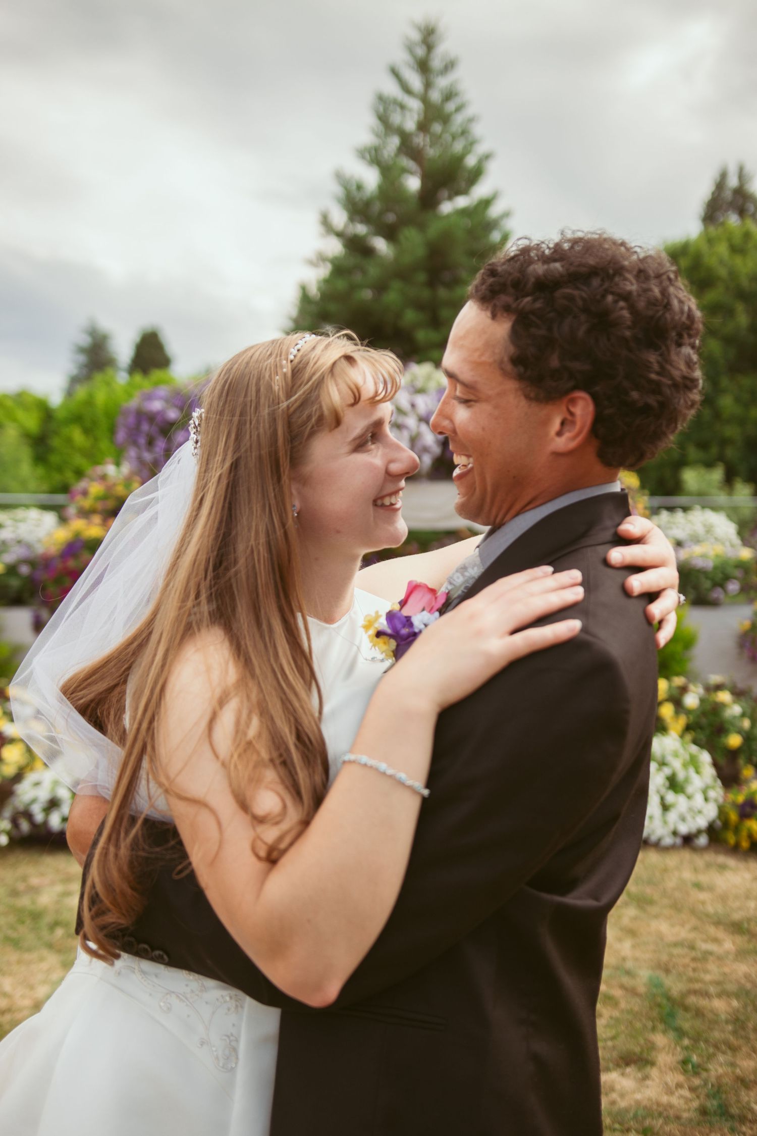 A couple shares a joyful laughing embrace during their outdoor garden wedding celebration.