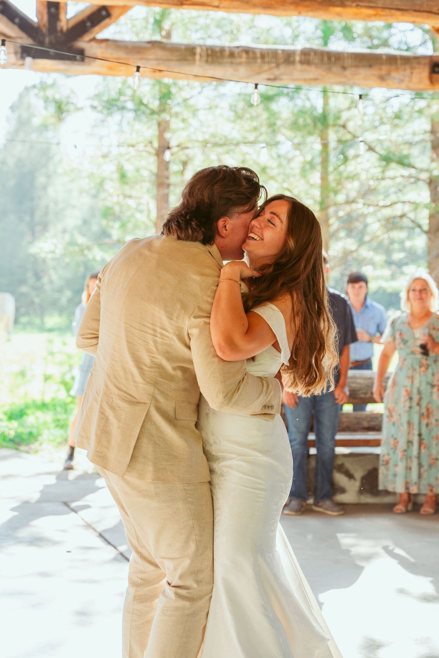 Couple embraces during romantic wedding dance in sunlit outdoor pavilion.