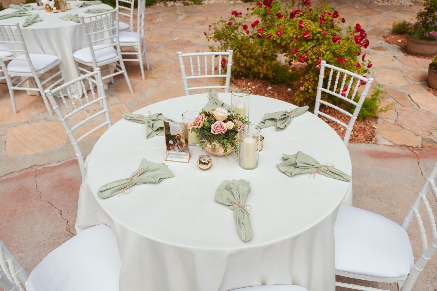 Elegant white table settings with floral centerpieces at an outdoor wedding reception.