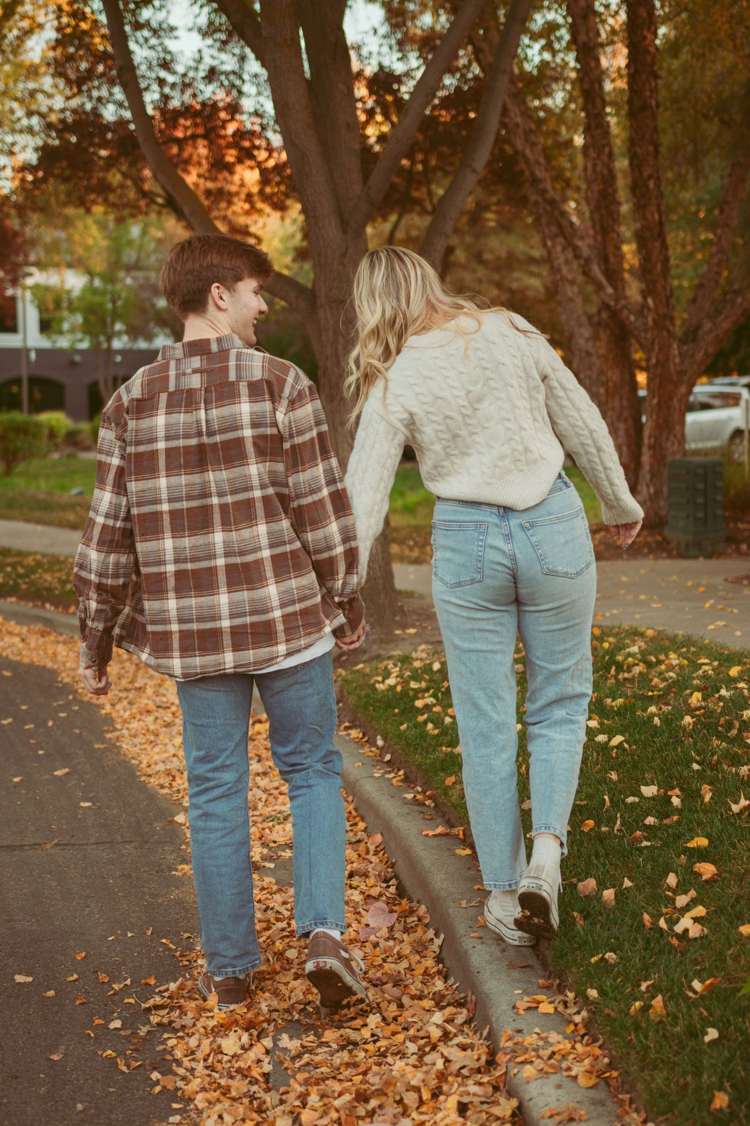 Couple walking through park with fallen autumn leaves beneath their feet.