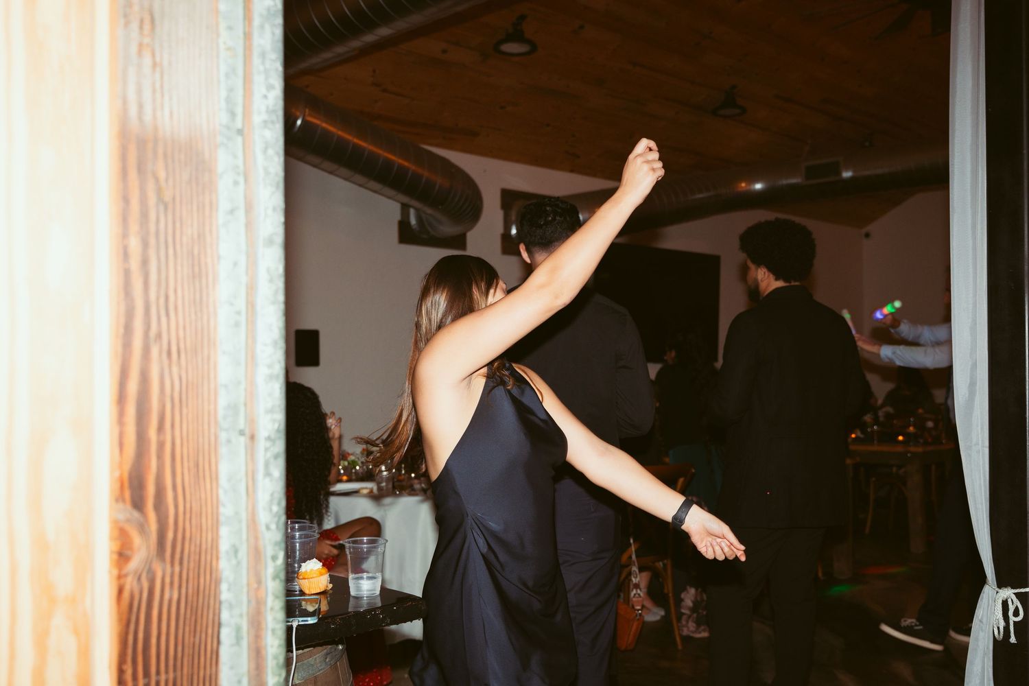 Dance floor silhouettes of party guests celebrating with raised arms under venue lighting.