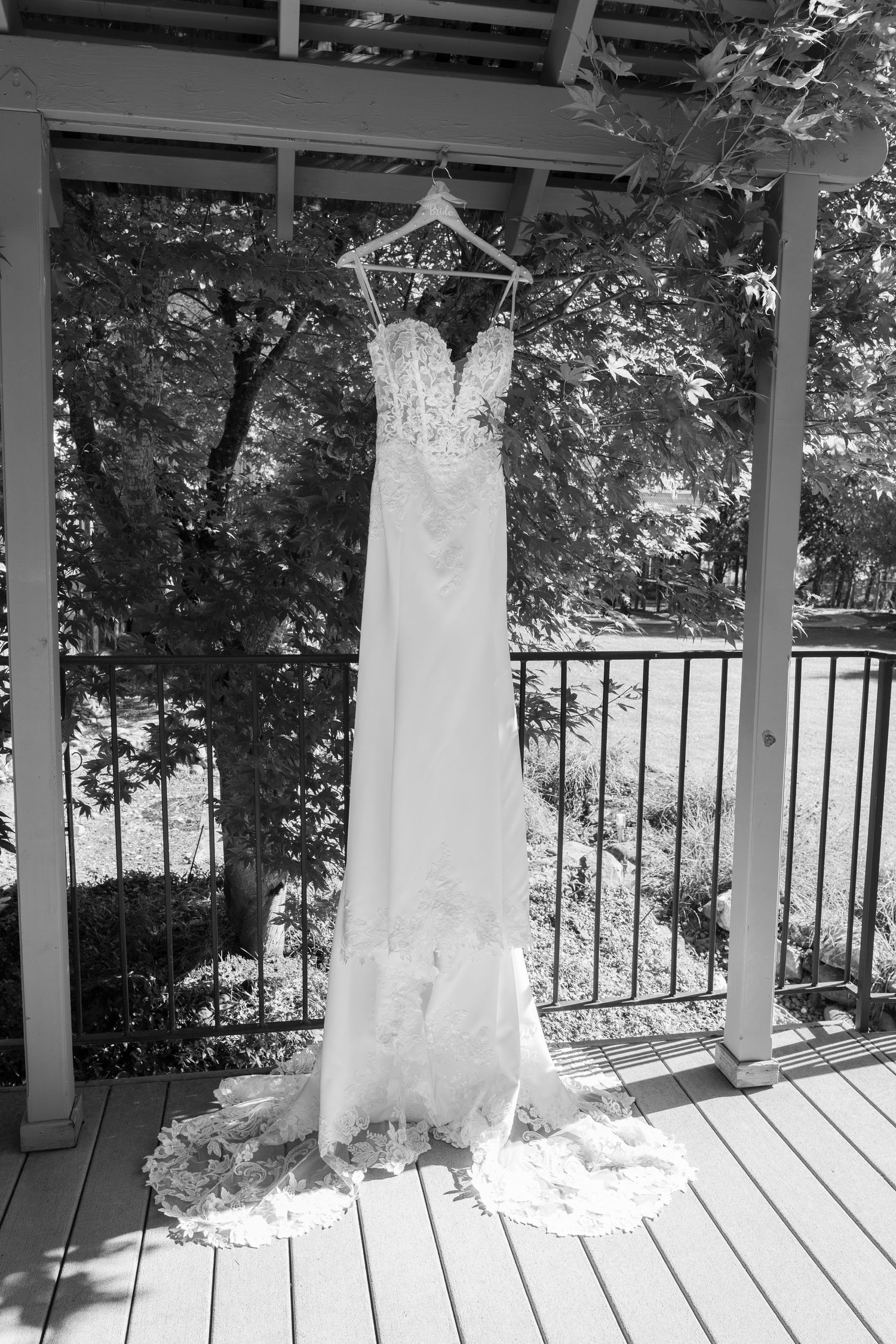 White lace wedding gown with sweetheart neckline displayed on hanger against outdoor deck railing.