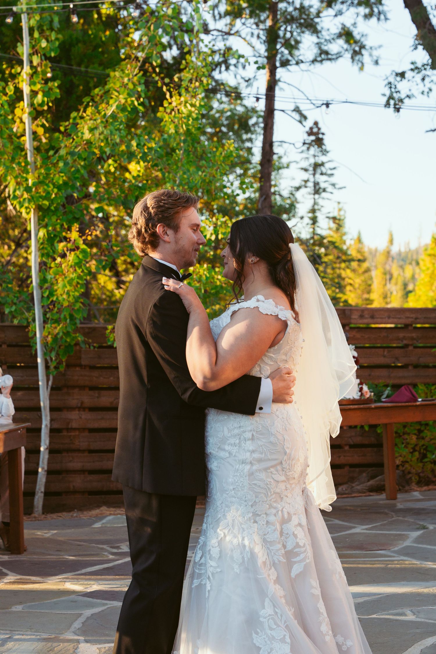 A couple shares an intimate dance moment at their outdoor wedding with string lights and trees.