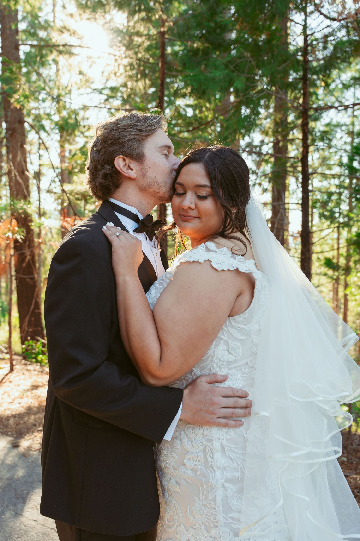 A sweet wedding moment captured in golden afternoon light among tall trees.