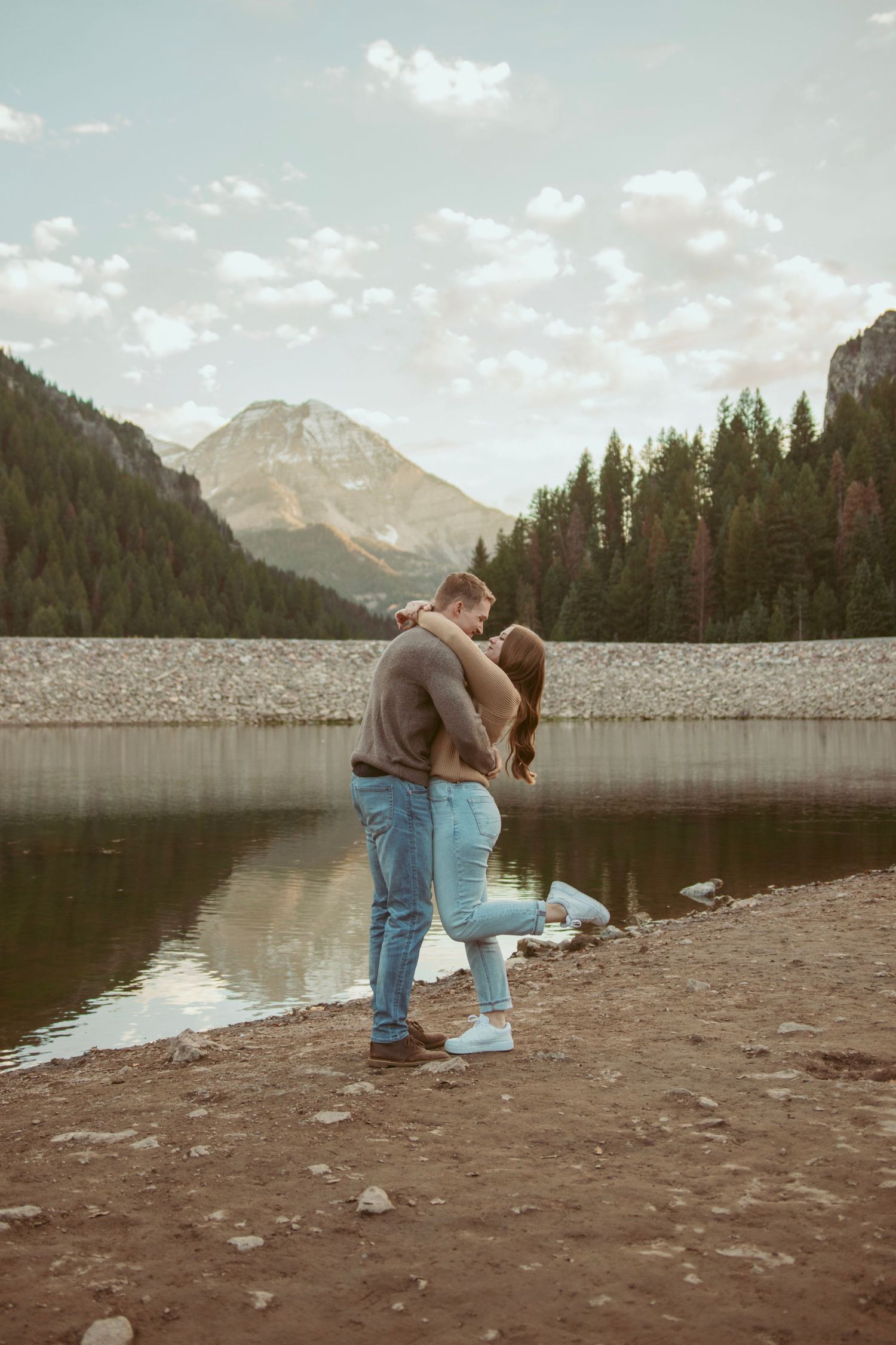 Couple sharing an intimate moment by a mountain reservoir with dramatic peaks in the background.