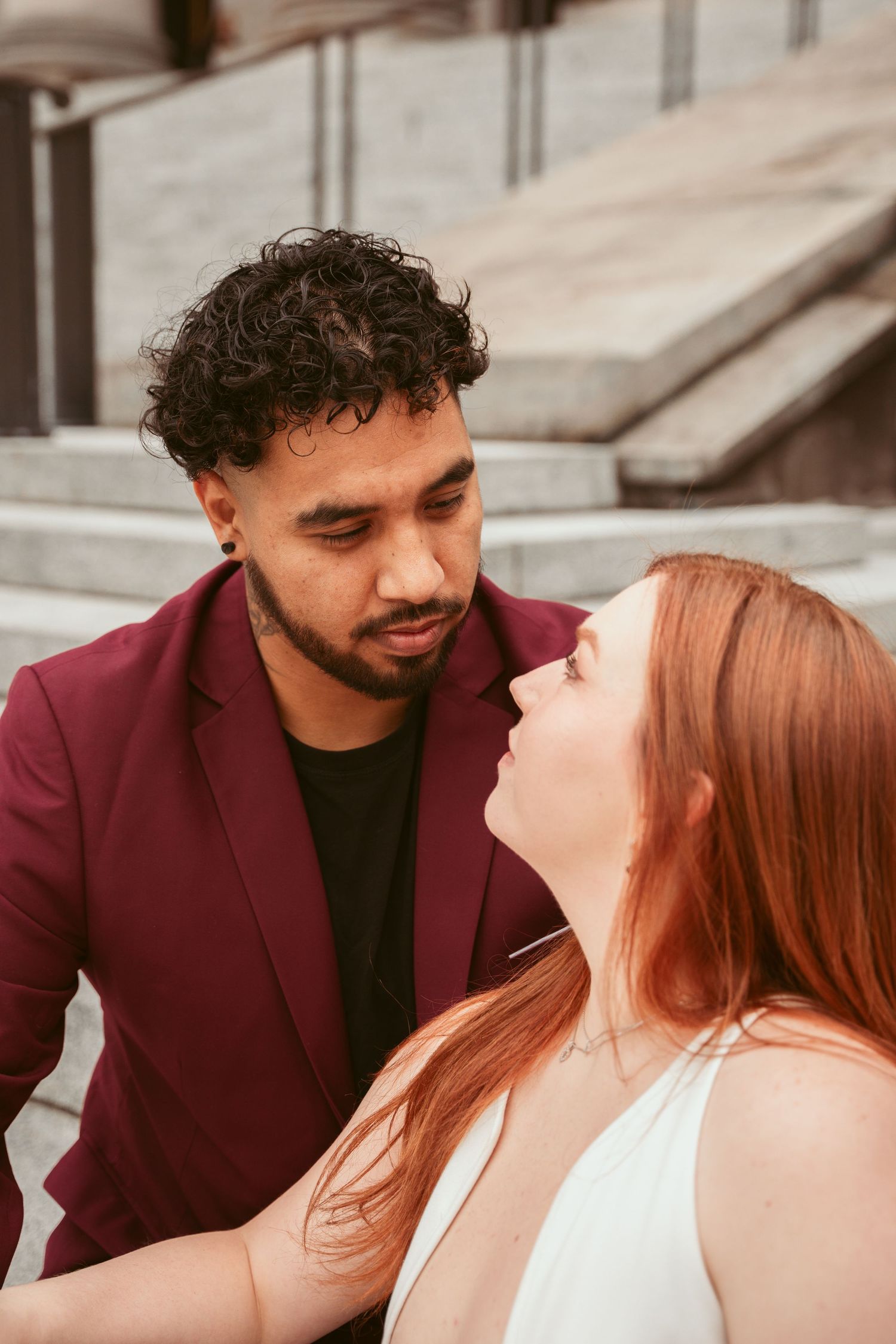 A close-up moment between a couple in burgundy and white against an urban backdrop.