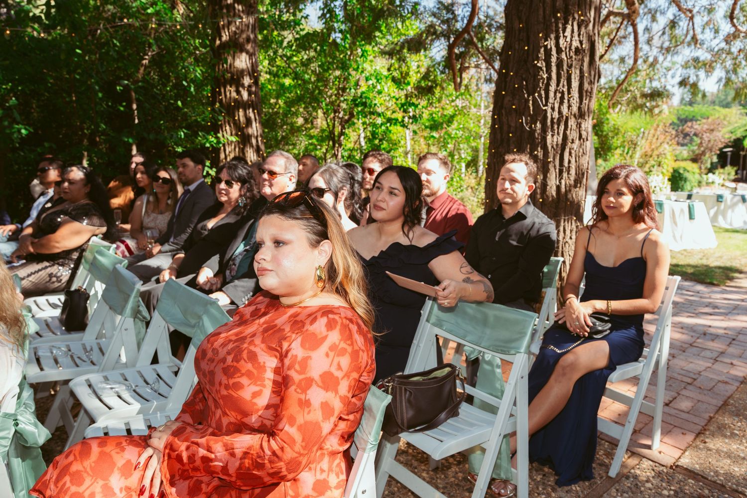 Wedding celebration under a wooden pavilion with guests seated on light blue chairs in an outdoor setting.