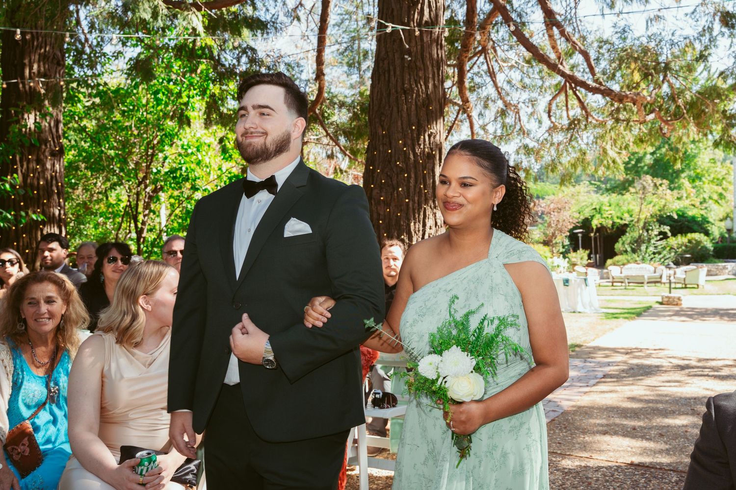 Guests gather under a rustic wooden pergola in a lush garden setting during an outdoor celebration.