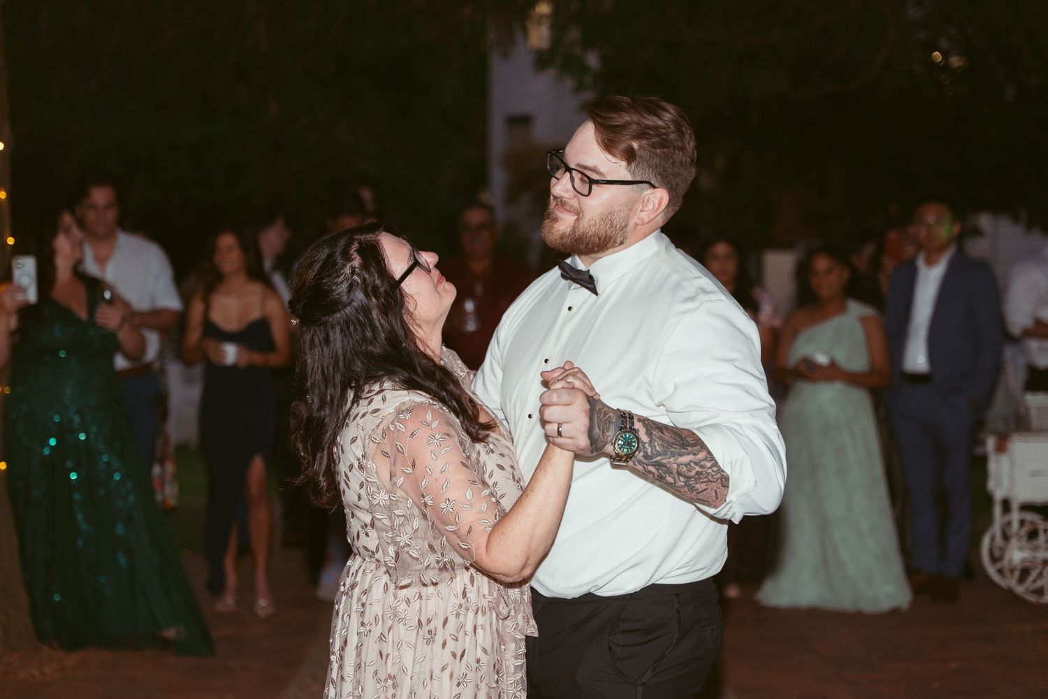 Couple shares intimate dance moment at outdoor wedding reception with string lights.