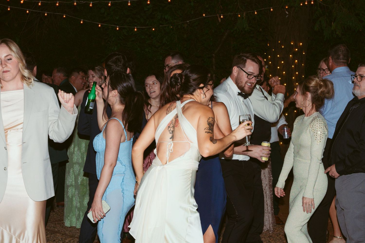 Wedding reception dance floor filled with guests under string lights.