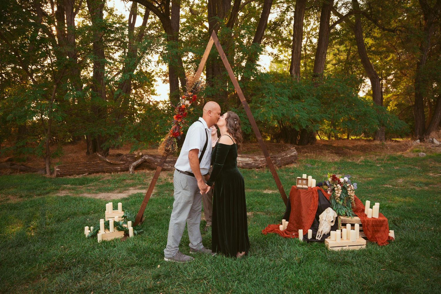A romantic outdoor wedding scene with wooden arch, candles, and decorative elements at sunset.