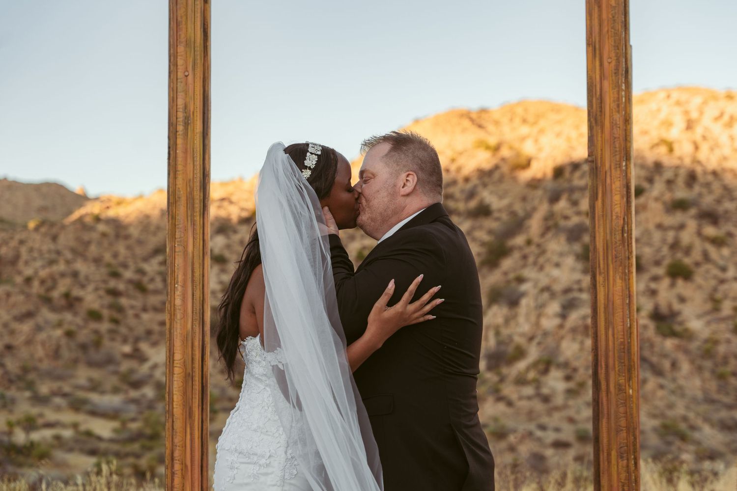 A couple dances together under a wooden arch with desert mountains behind them.