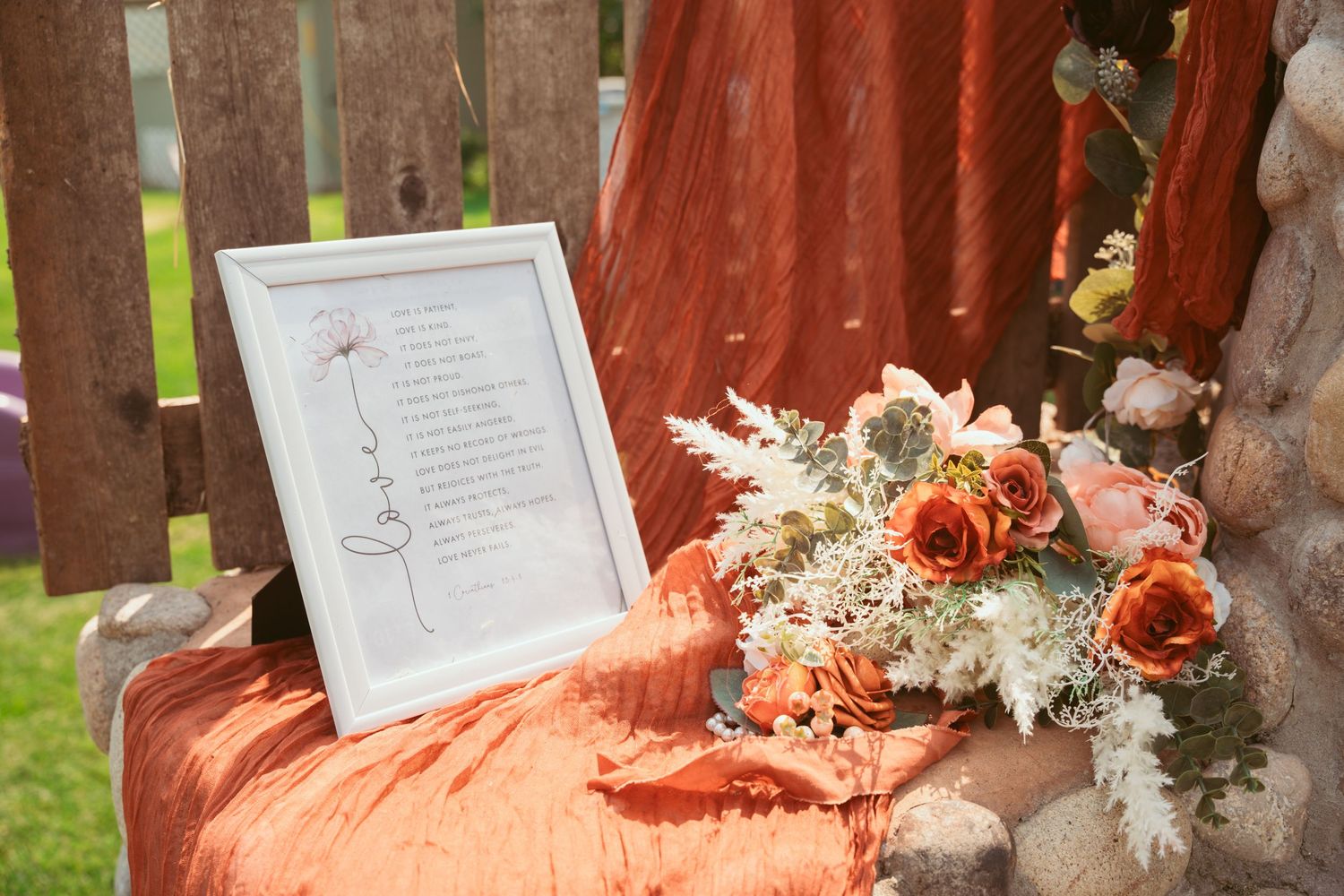 Wedding details displayed on a rustic table with coral-colored fabric and floral arrangements.