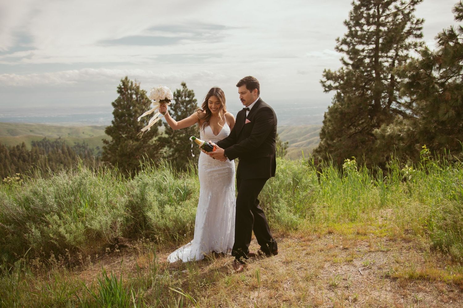 Wedding couple toasts with champagne glasses against a scenic mountain backdrop.