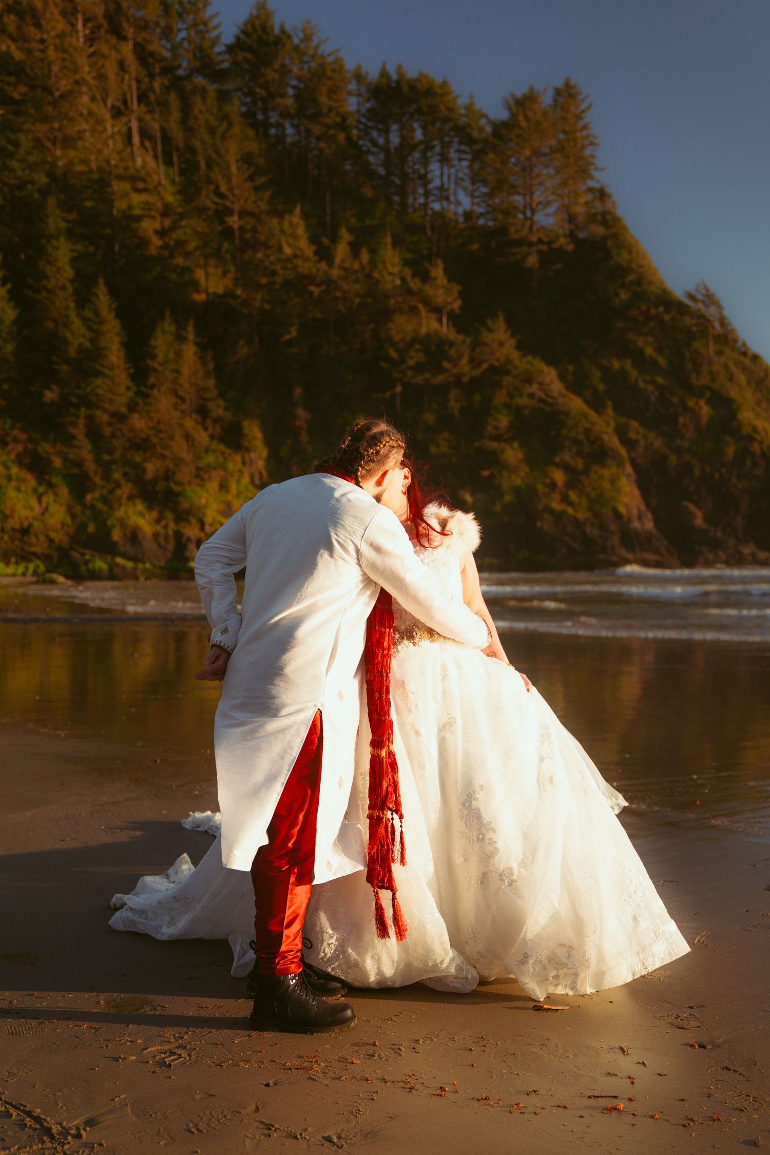 Wedding couple sharing an intimate moment on a beach with dramatic cliffs in the background.