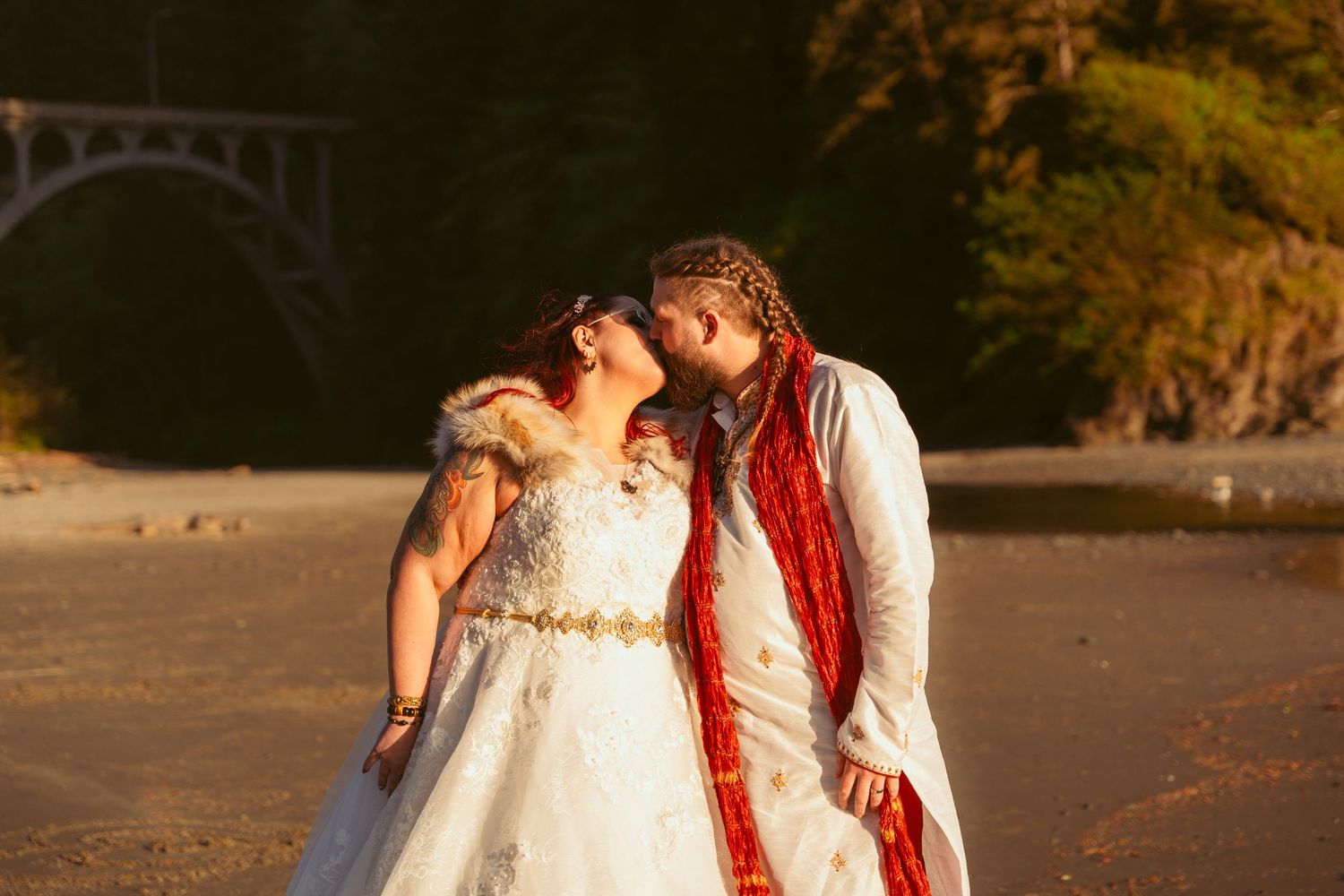 Intimate beach wedding portraits at golden hour with evergreen forest backdrop.