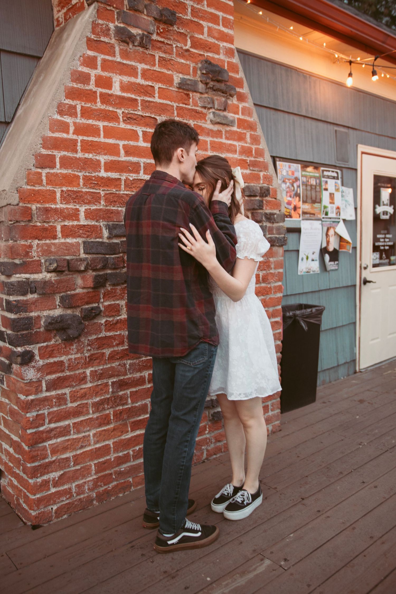 Couple sharing an intimate moment along a brick building with string lights.