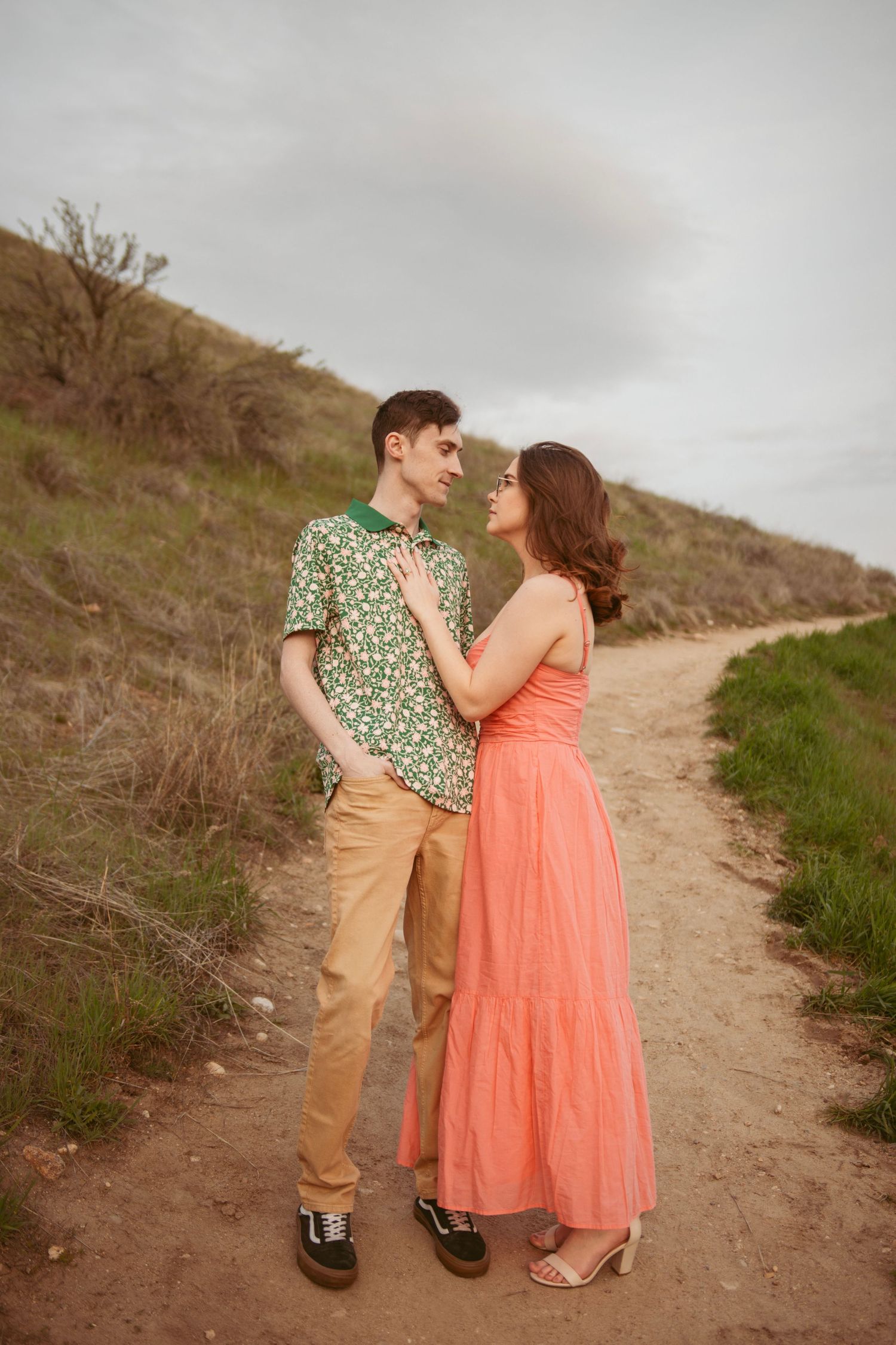A couple in spring attire poses together on a dirt hiking trail.