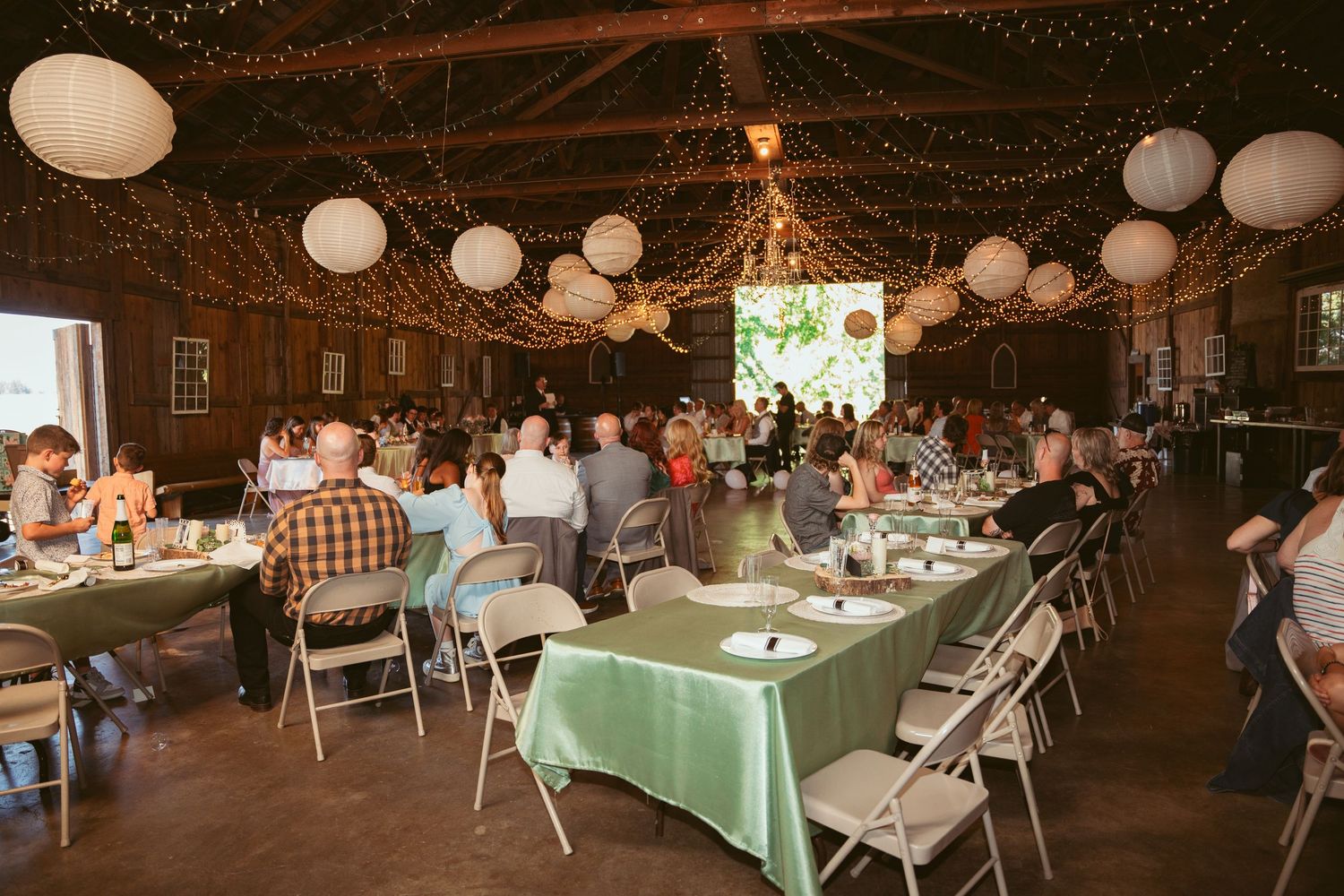 Barn wedding reception with mint green tablecloths and white paper lanterns hanging from wooden beams.