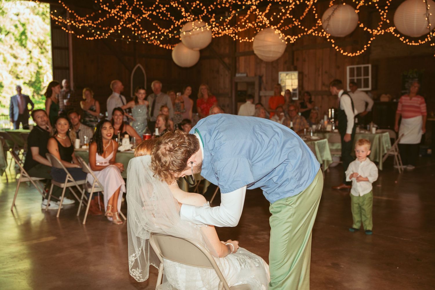 Rustic barn wedding reception with guests dancing beneath glowing lights and paper lanterns.