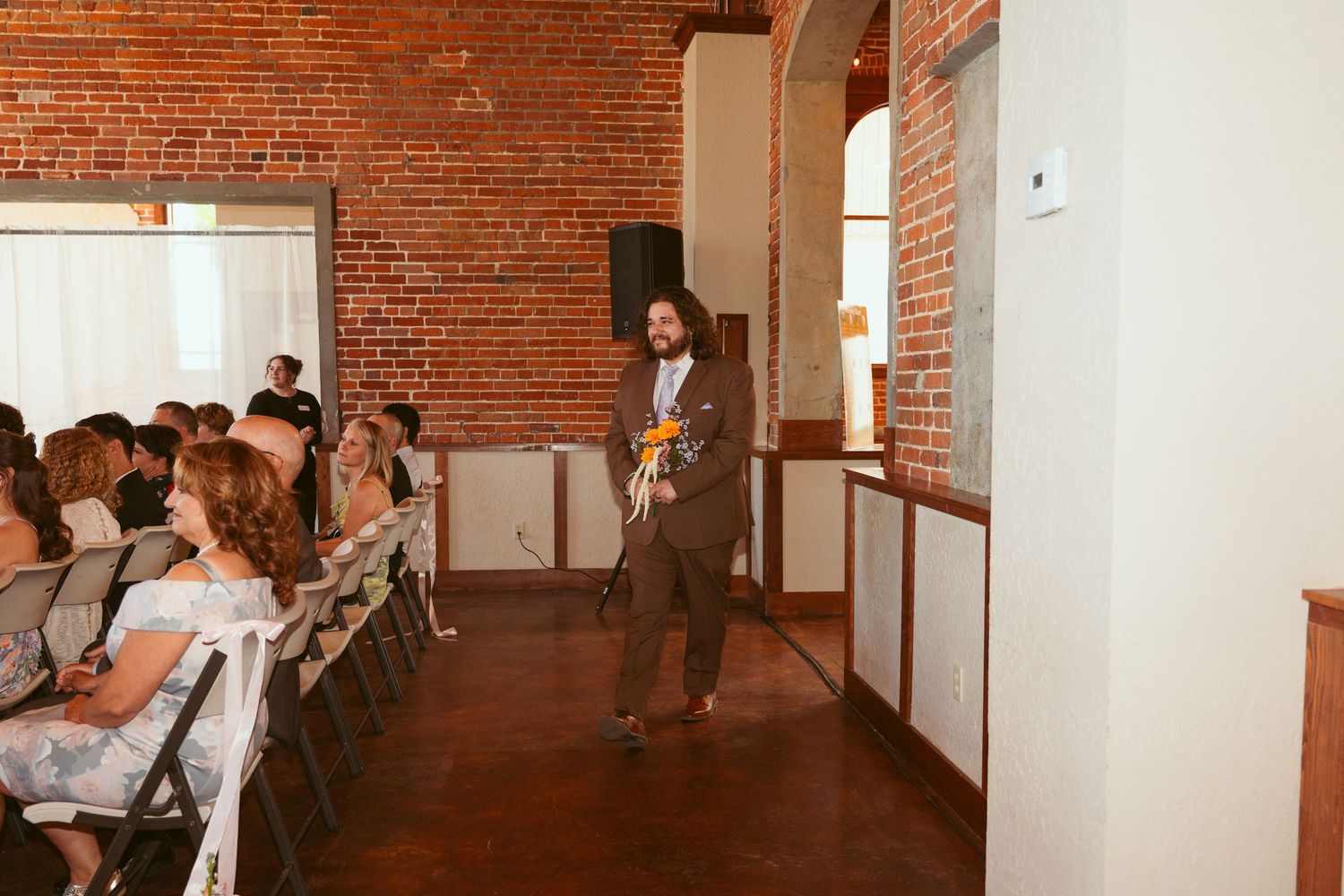 Wedding ceremony taking place in a converted industrial space with exposed brick walls and natural lighting.