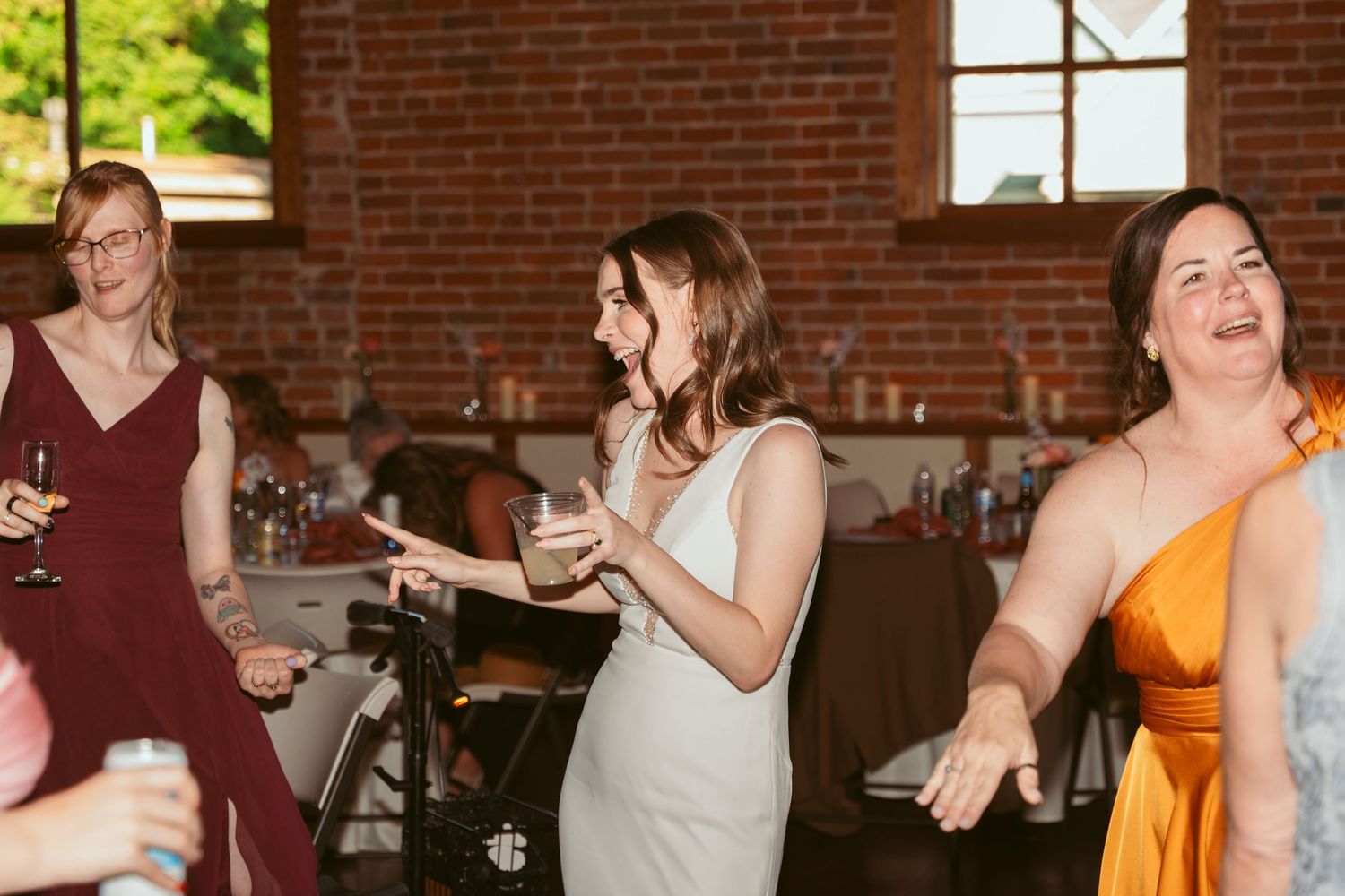 Wedding reception dance party in a historic brick building with natural light streaming through windows.